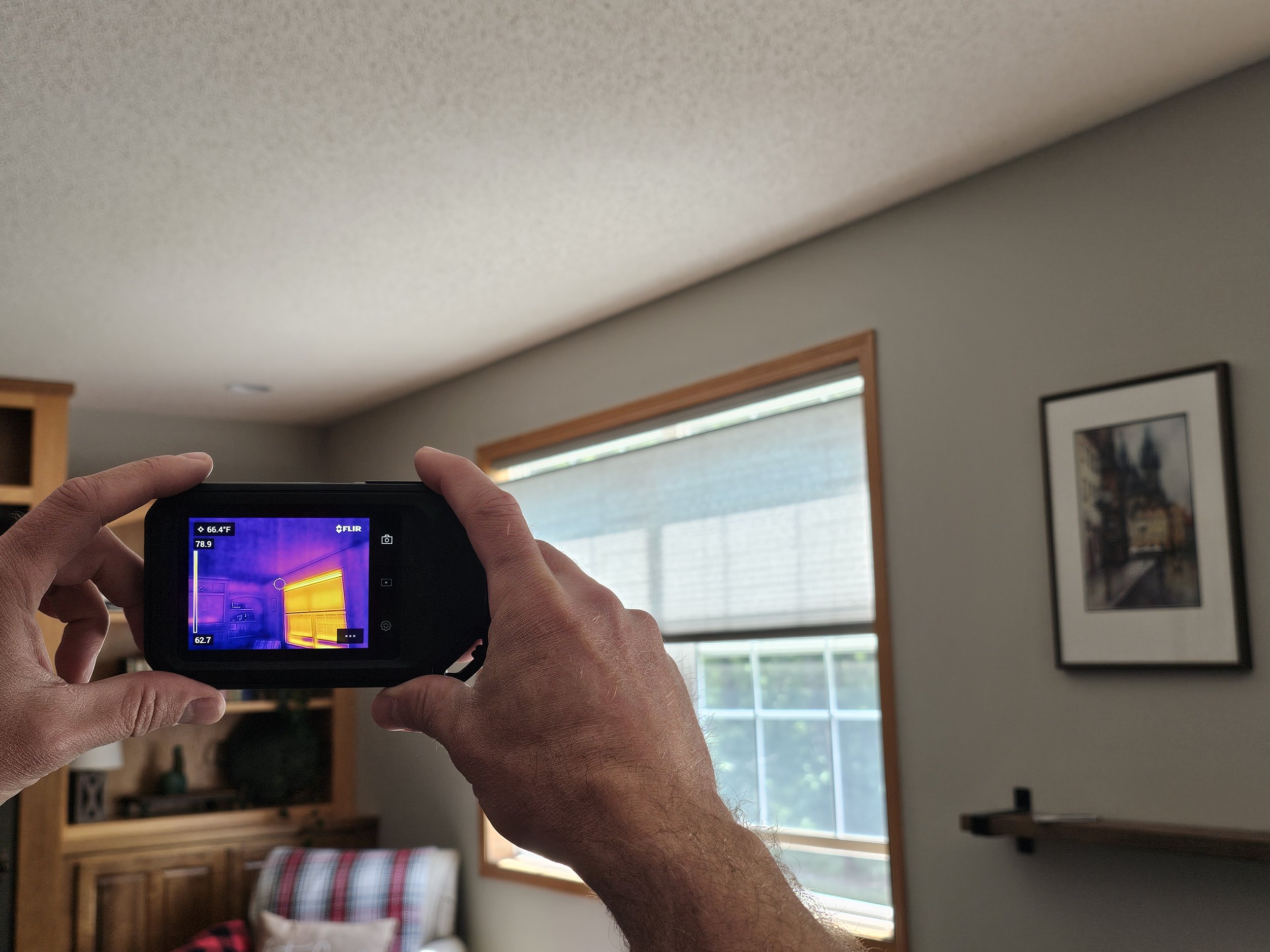 Close-up thermal camera image showing a large area of energy loss (hot colors) around an interior window frame, indicating missing wall insulation or a significant air draft.