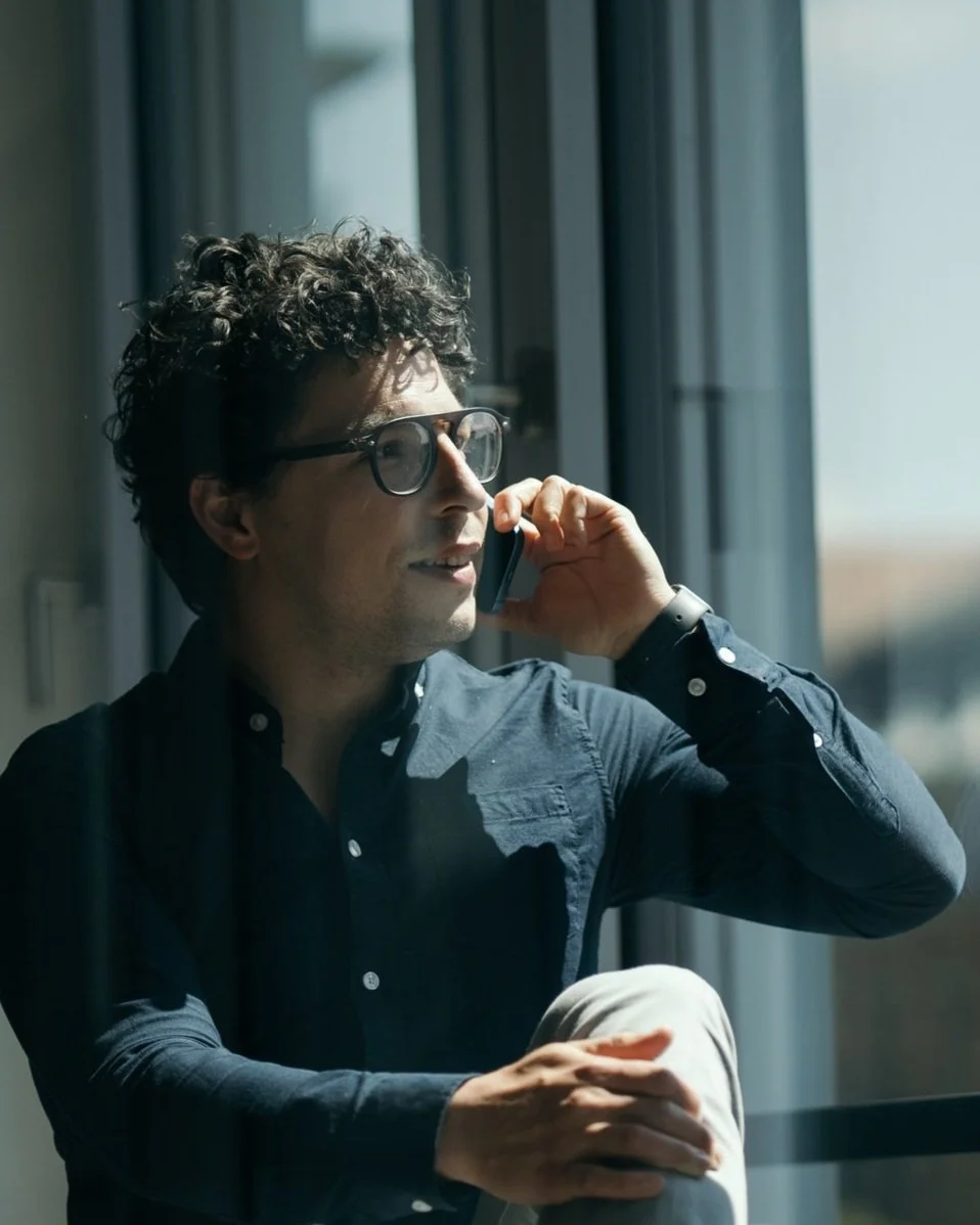 Noel Bossart, CEO von Noevu mit 25 Jahren Erfahrung: Mann mit Locken, Brille und dunklem Hemd sitzt am Fenster, telefoniert und blickt nach draussen.