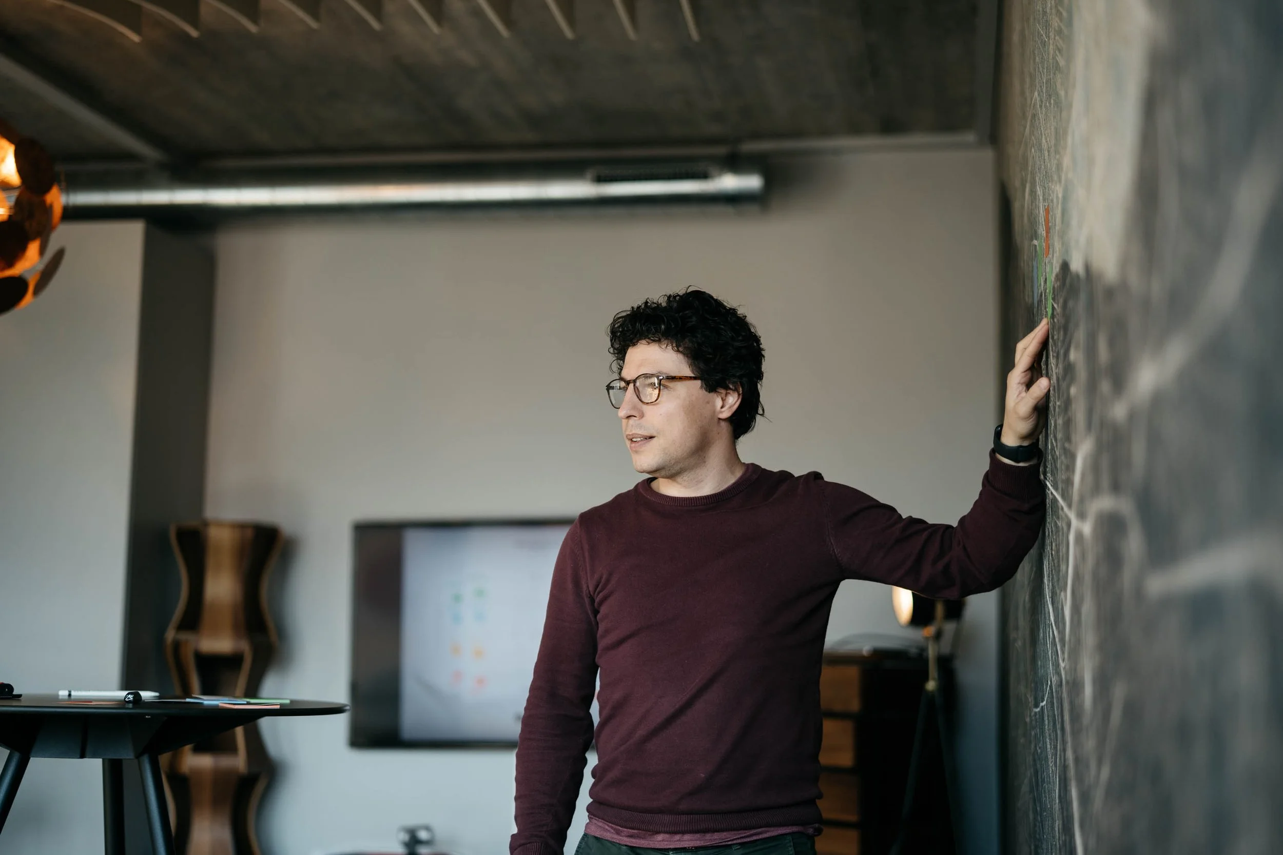 Noel Bossart, CEO of Noevu with 25 years of experience: a man with curly hair, glasses and a dark shirt sits by the window, talking on the phone and looking out.