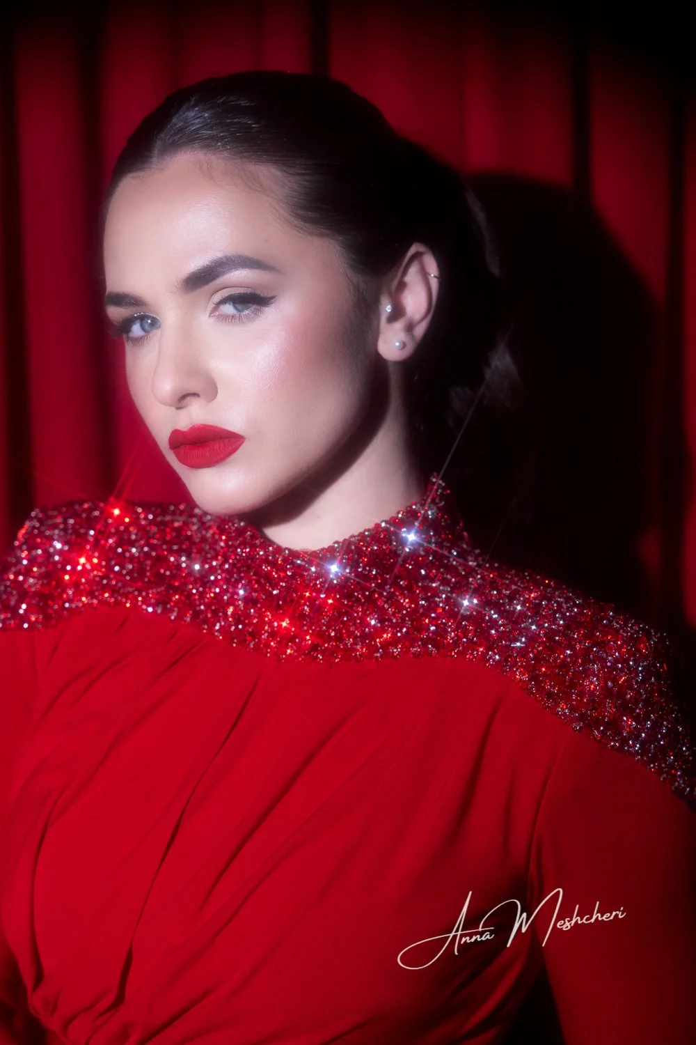Hollywood glam beauty portrait featuring a model in a red embellished gown with sparkling in-camera starburst effects against a dramatic red studio backdrop.