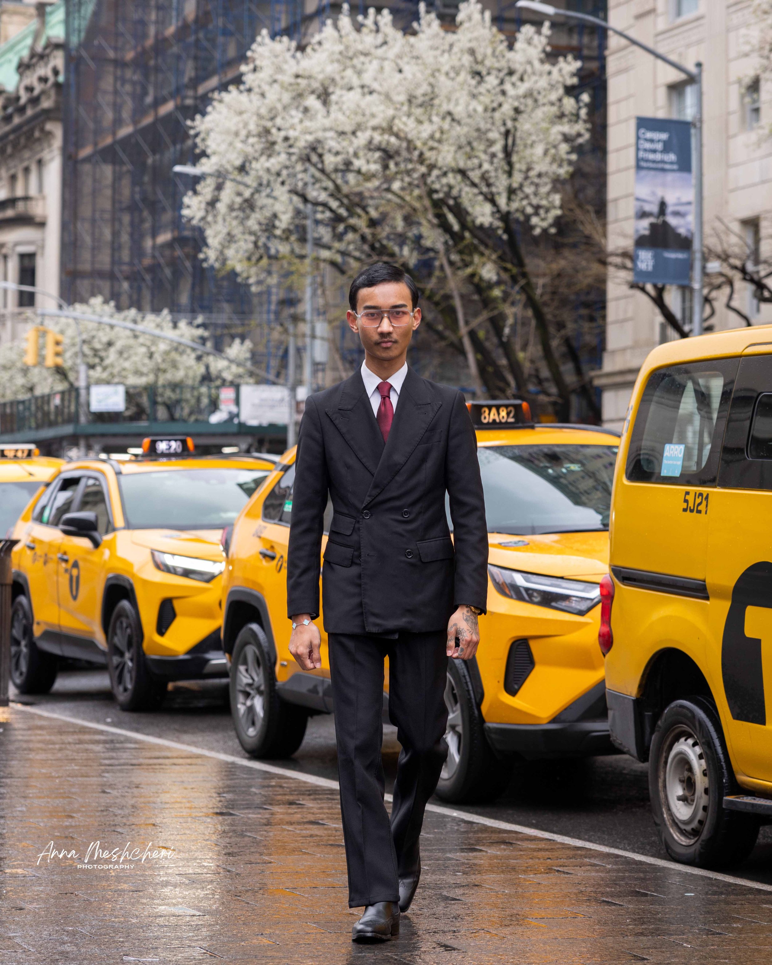 A man walking in a street of New York with yellow taxi cabs behind him