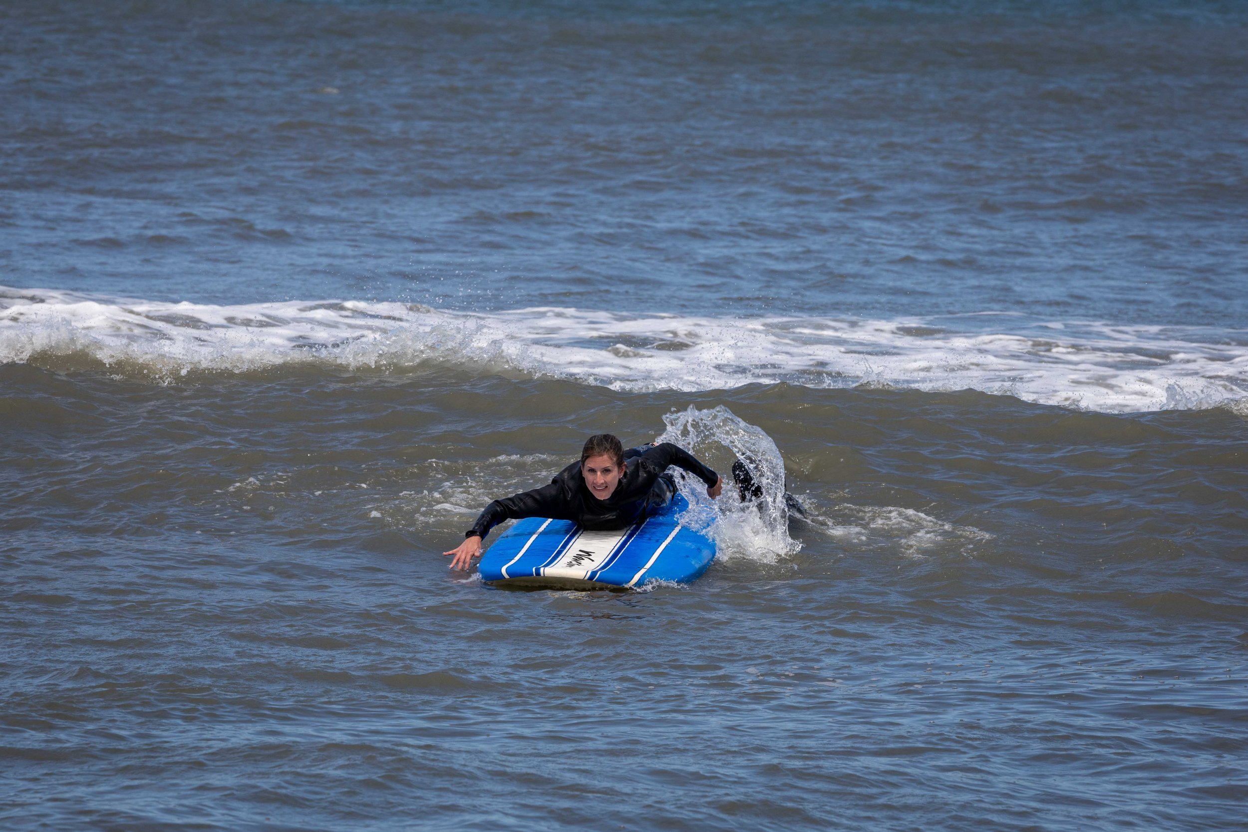 Person in a wetsuit riding a blue surfboard on ocean waves.
