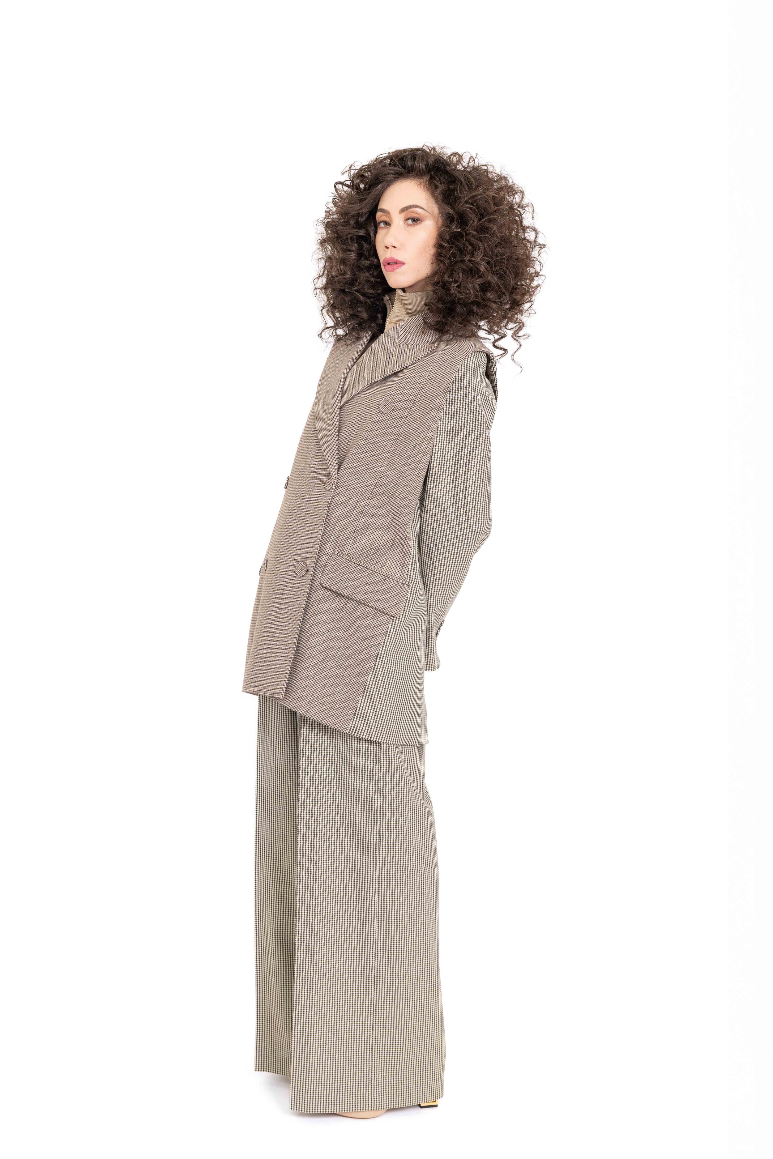 Woman with curly hair wearing a houndstooth patterned suit standing against a white background. Catalogue Photography. Brand: Fendi. Photographed by Anna Meshcheri