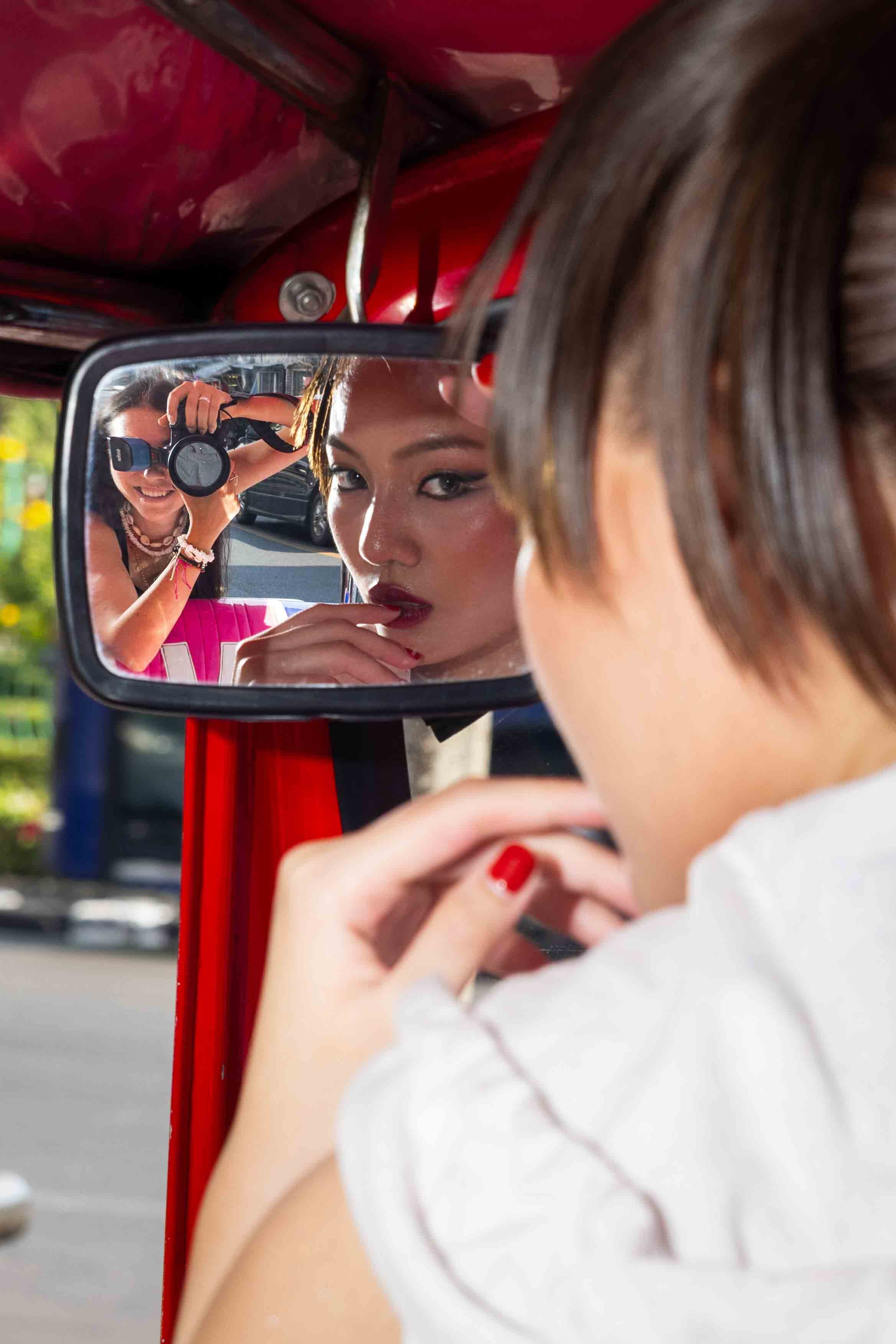 Woman looking at herself in a mirror with another person photographing her reflection. Bangkok Fashion Editorial photoshoot by Anna Meshcheri