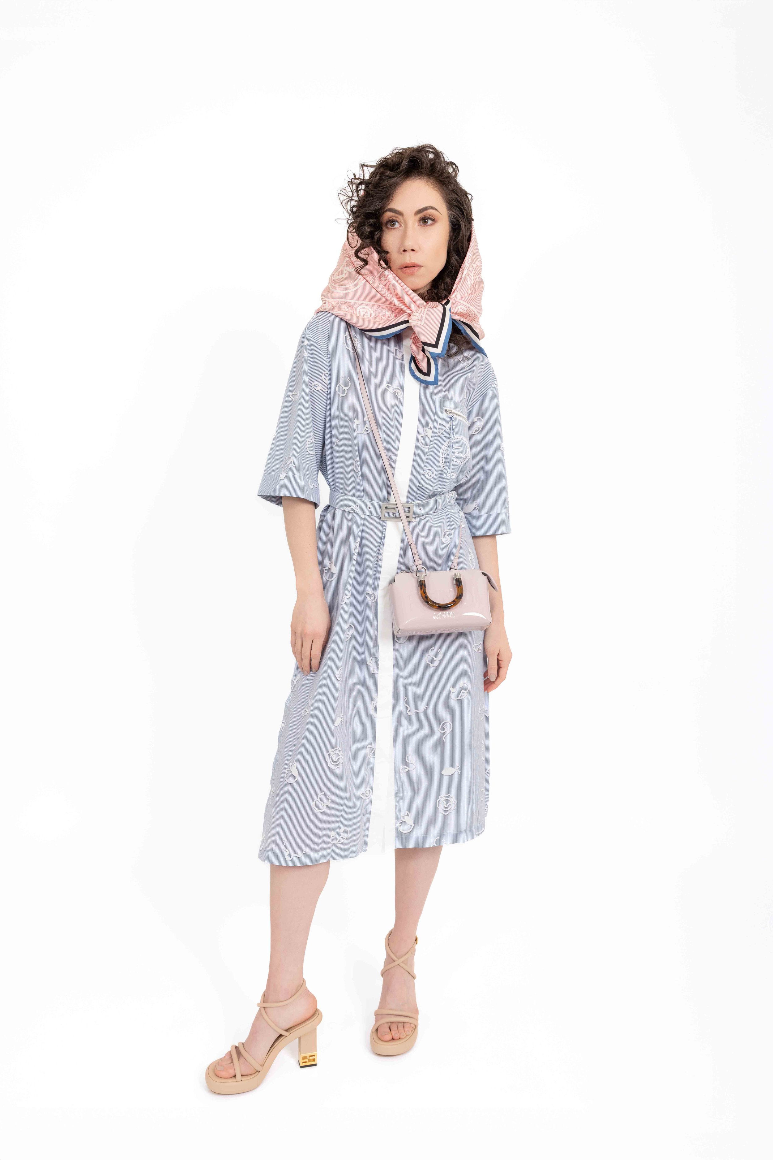 Woman wearing a blue patterned dress, pink headscarf, crossbody bag, and beige sandals. Catalogue Photography. Brand: Fendi. Photographed by Anna Meshcheri
