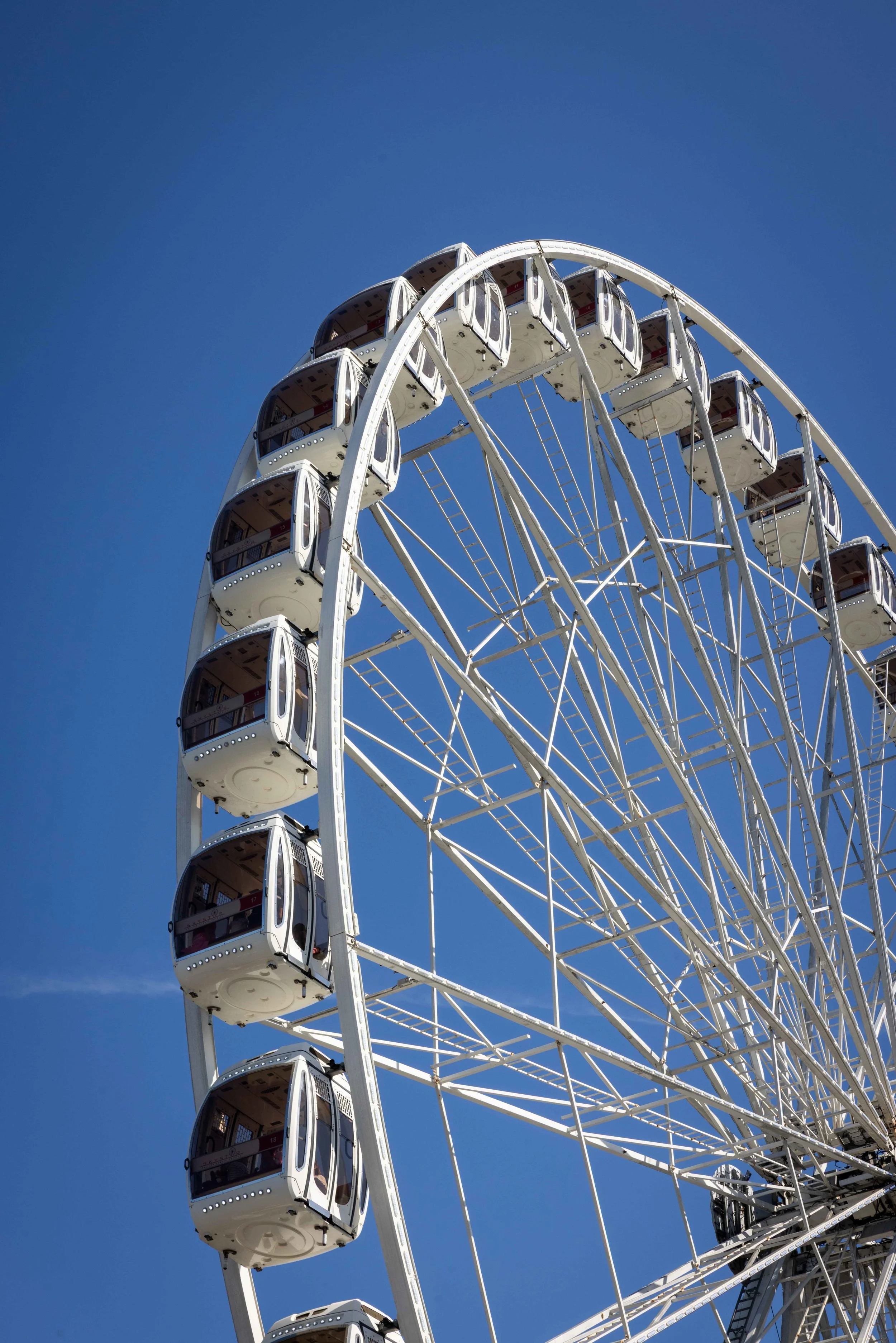 Close-up of a large Ferris wheel with white cabins against a clear blue sky.