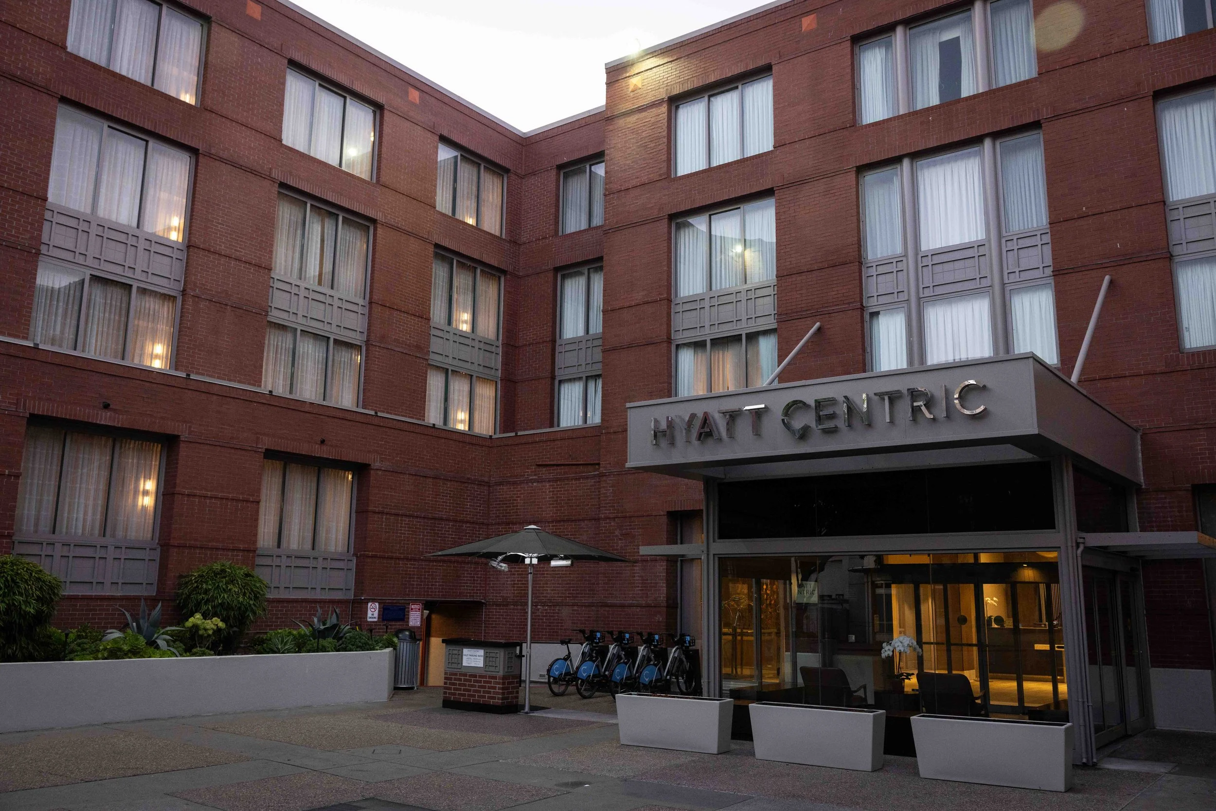 The exterior of the Hyatt Centric hotel building with multiple apartment windows, a small outdoor seating area, and a row of bicycles parked in front.