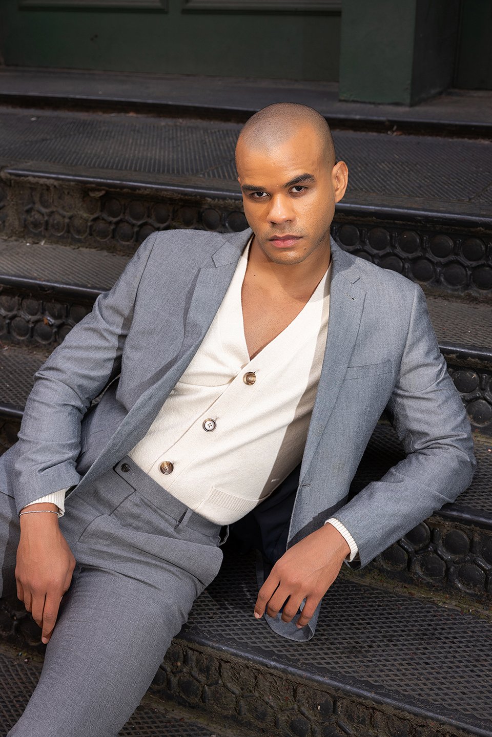 A man wearing a gray suit sitting on stairs, posing for a lifestyle photoshoot