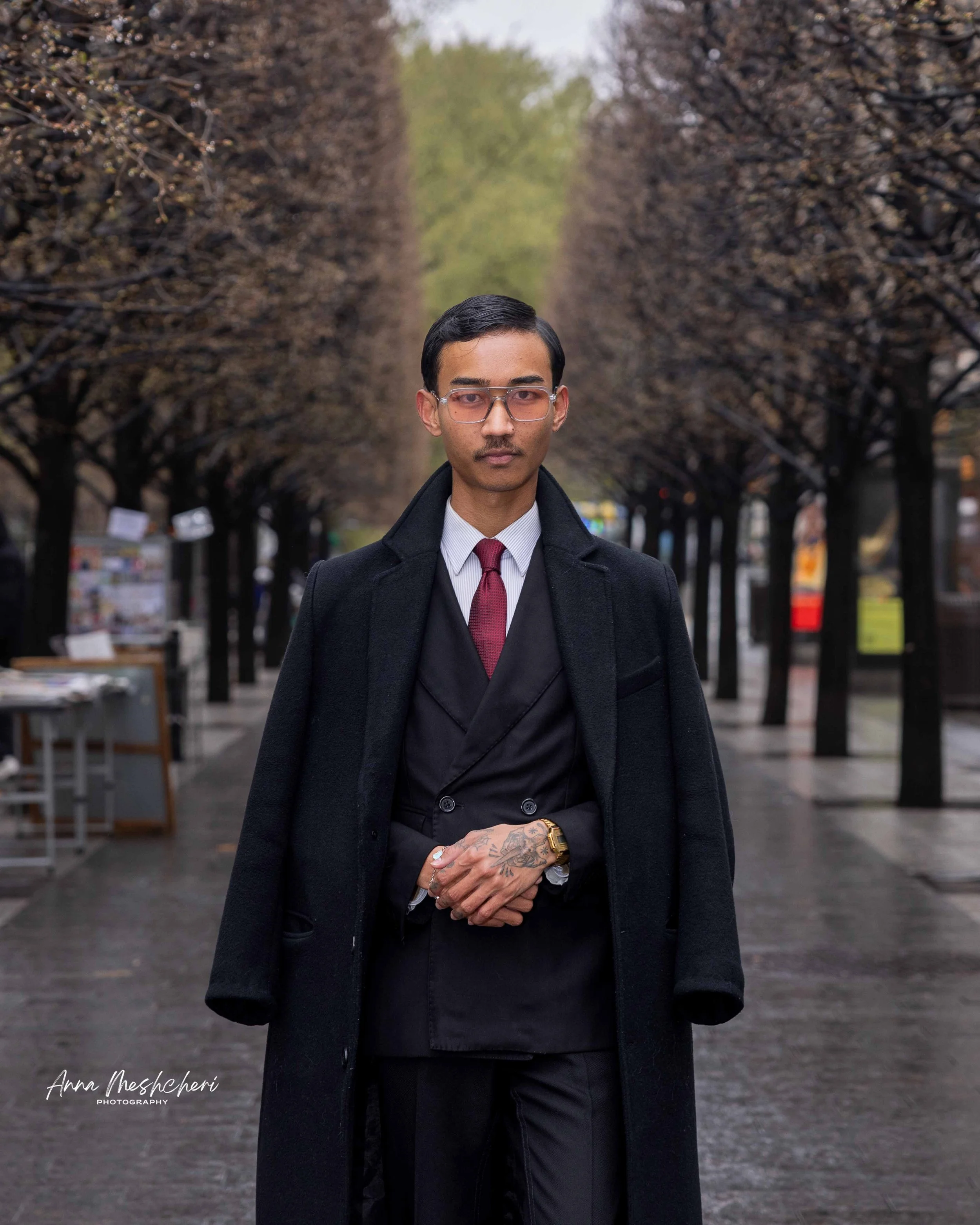 A man posing in a black suit and a black coat in an alley near the Metropolitan museum of art