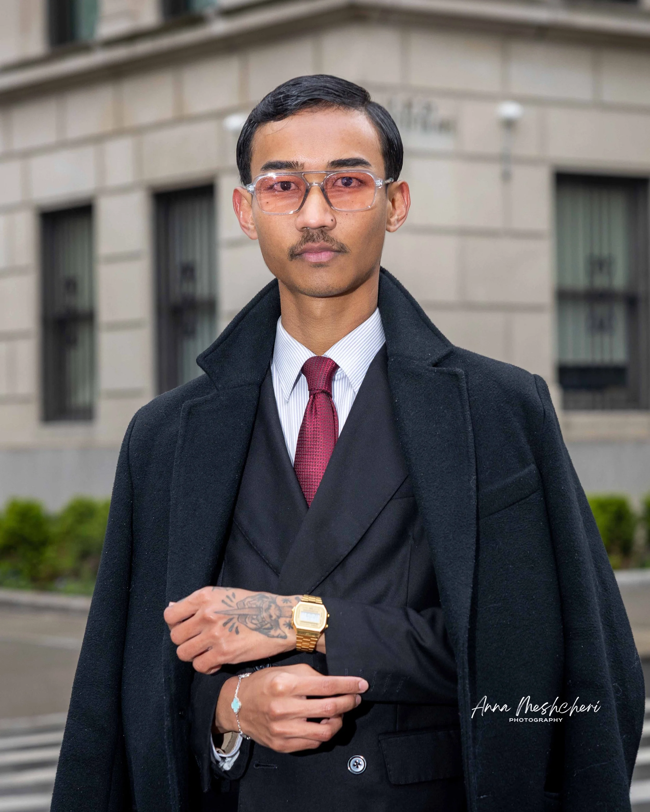 A man posing in a black suit and a black coat in a street of New York