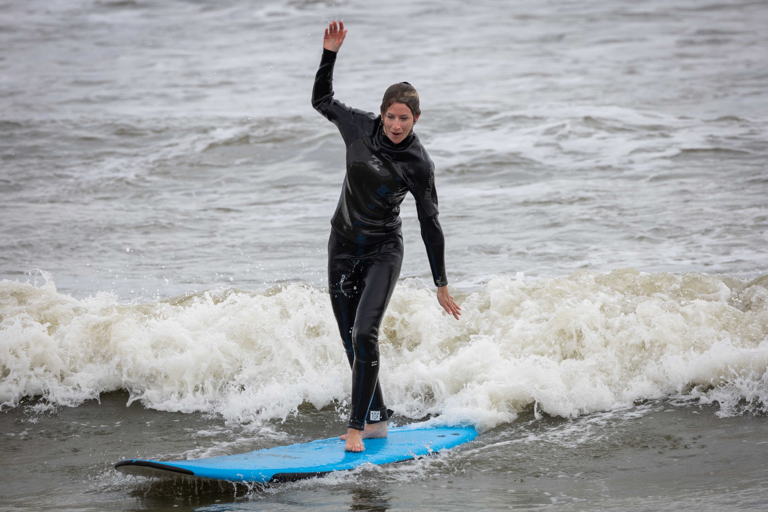 Person surfing on a blue surfboard in the ocean, wearing a black wetsuit.