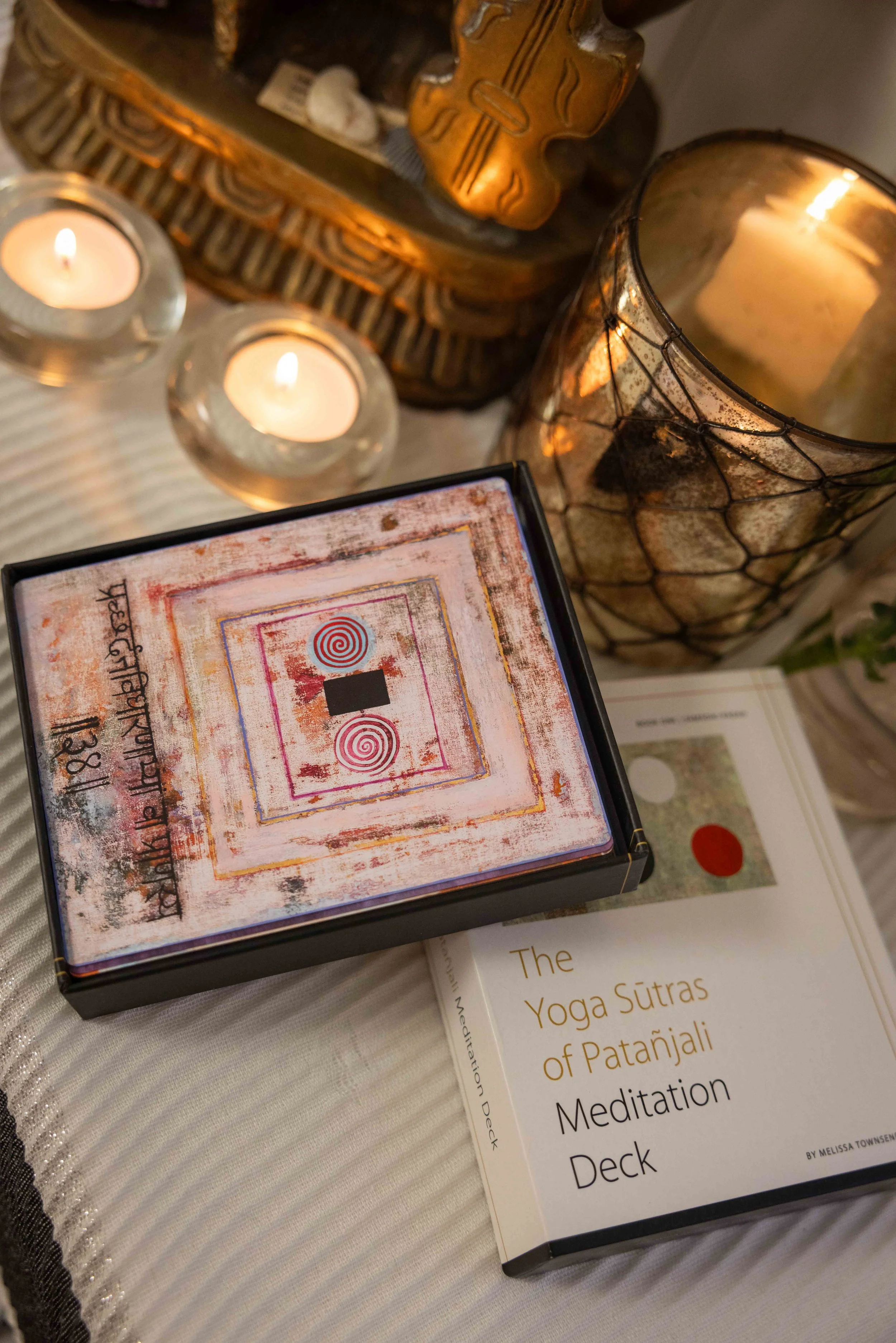 Close-up view of a book titled 'The Yoga Sutras of Patañjali' on meditation deck, surrounded by candles and decorative items on a table.