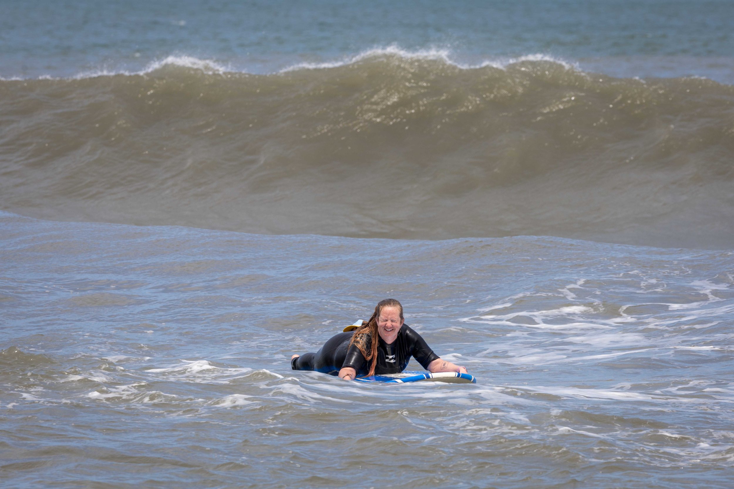 Person surfing on a blue surfboard in the ocean with large waves in the background.