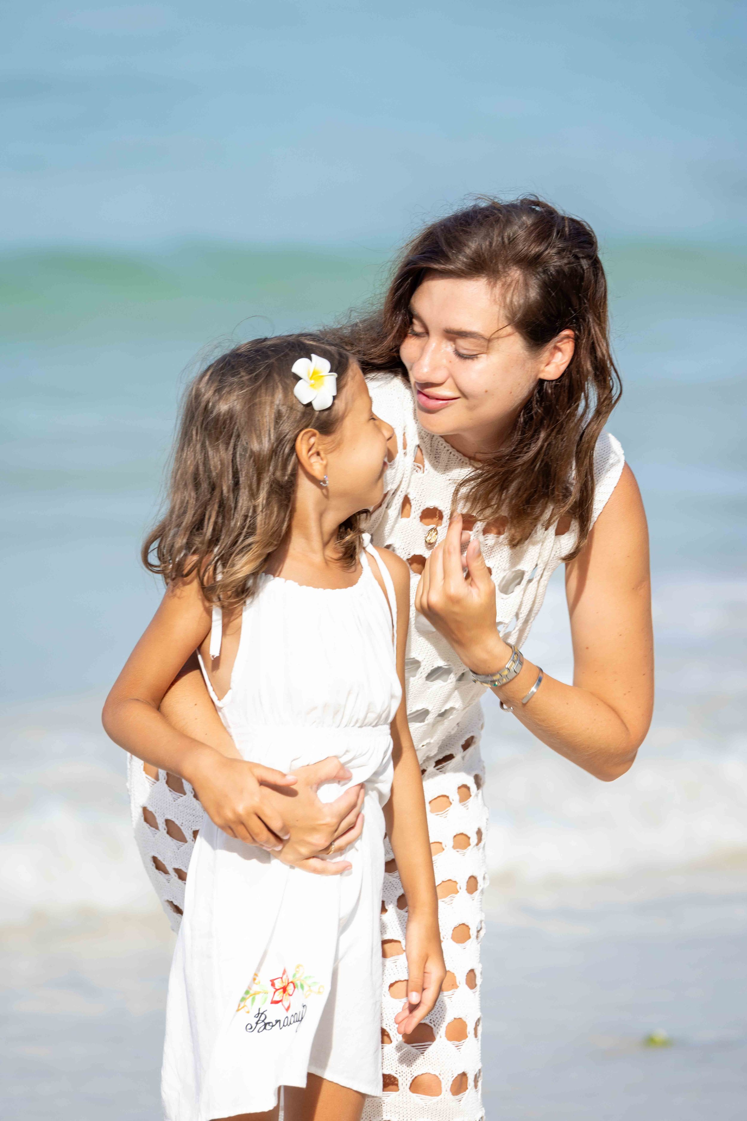 A woman and a child in white dresses, smiling at each other on a beach. Boracay beach lifestyle family photoshoot by Anna Meshcheri
