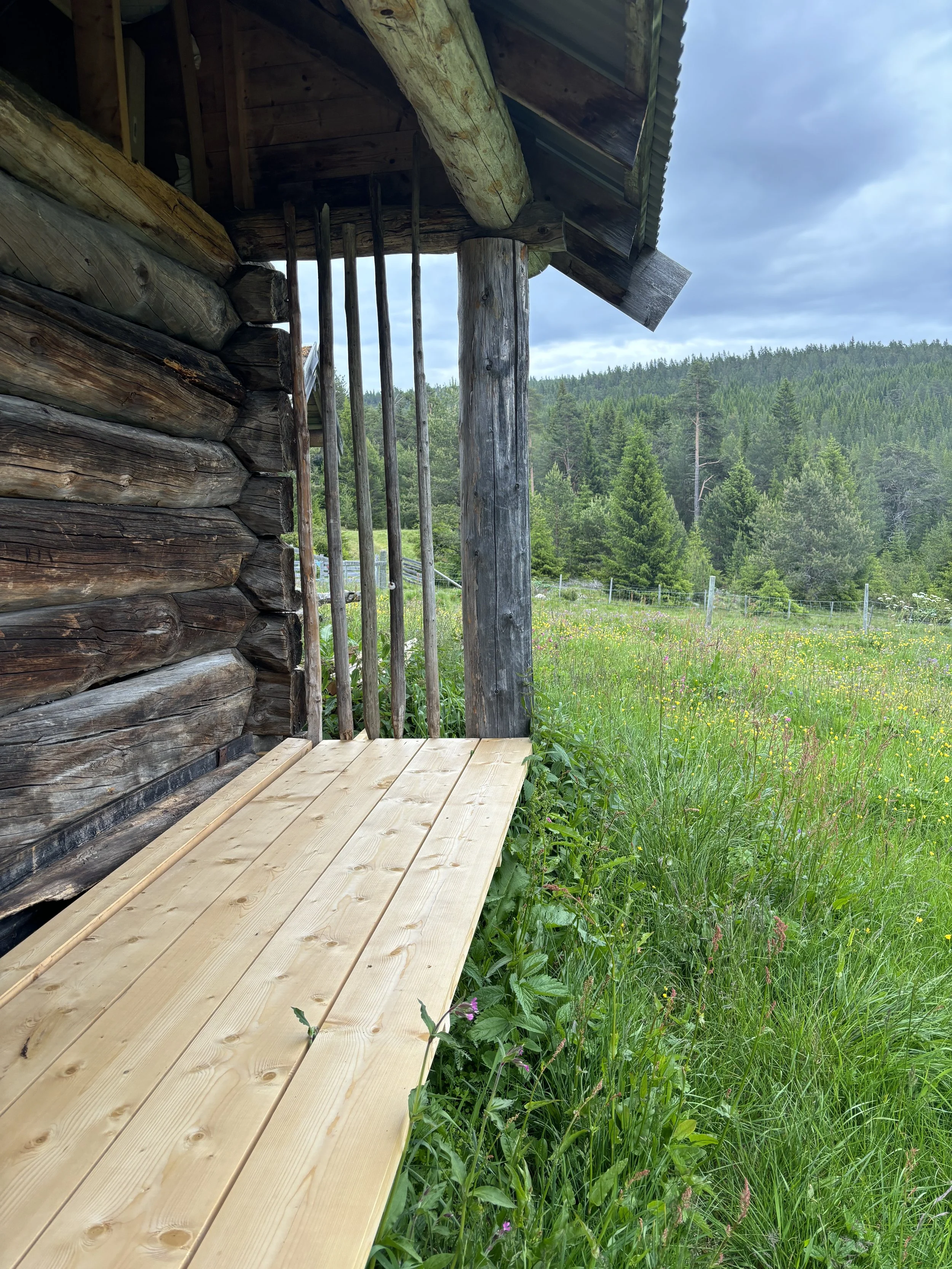 En utvendig veranda er satt der den gamle laftveggen er inntrukket fra fasadelivet. Den gir plass til frokost under tak, med utsikt i sol og regn.
