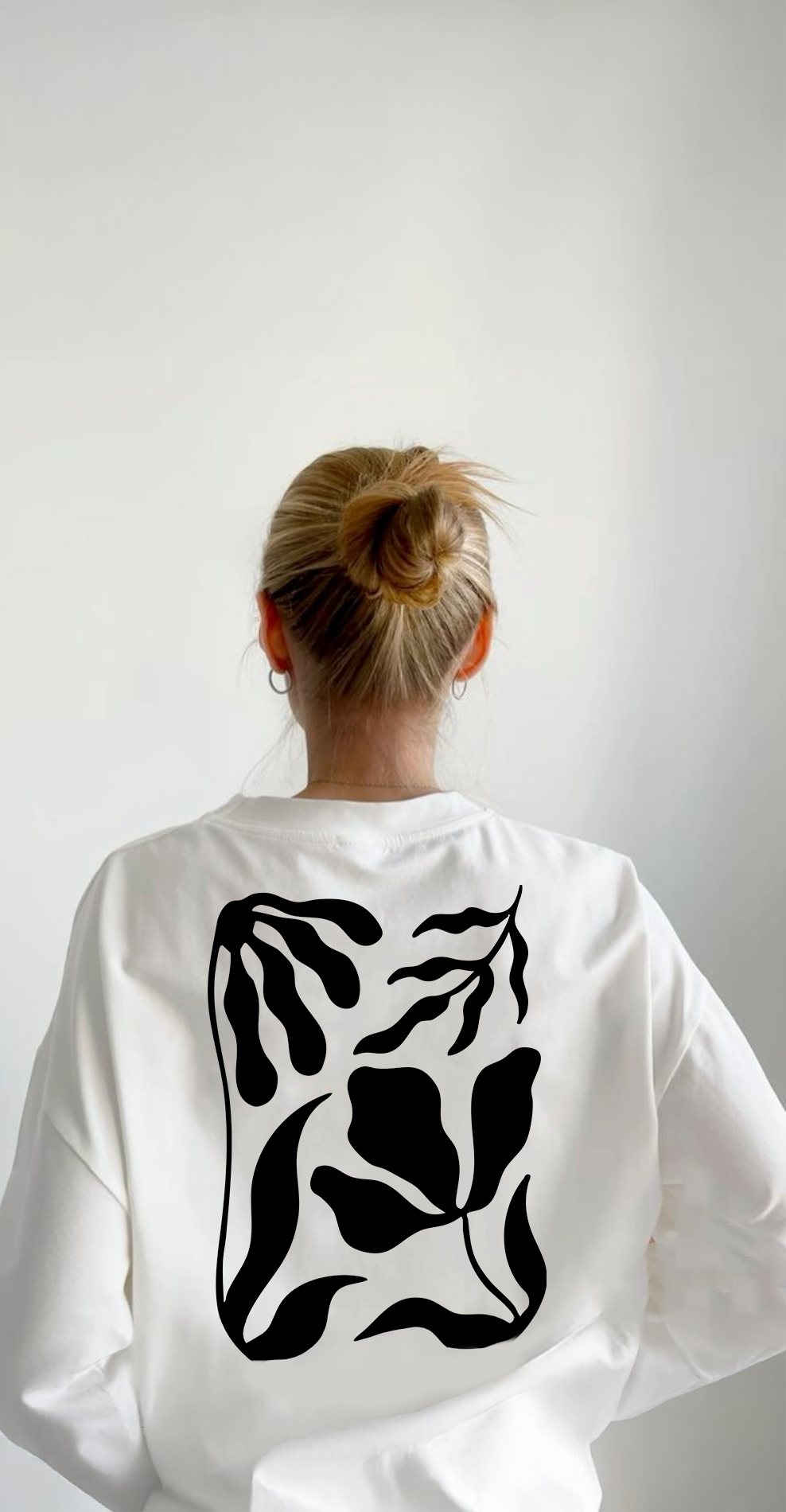 Back of a woman with blonde hair in a bun, wearing a white sweatshirt with black abstract line art design on the back.