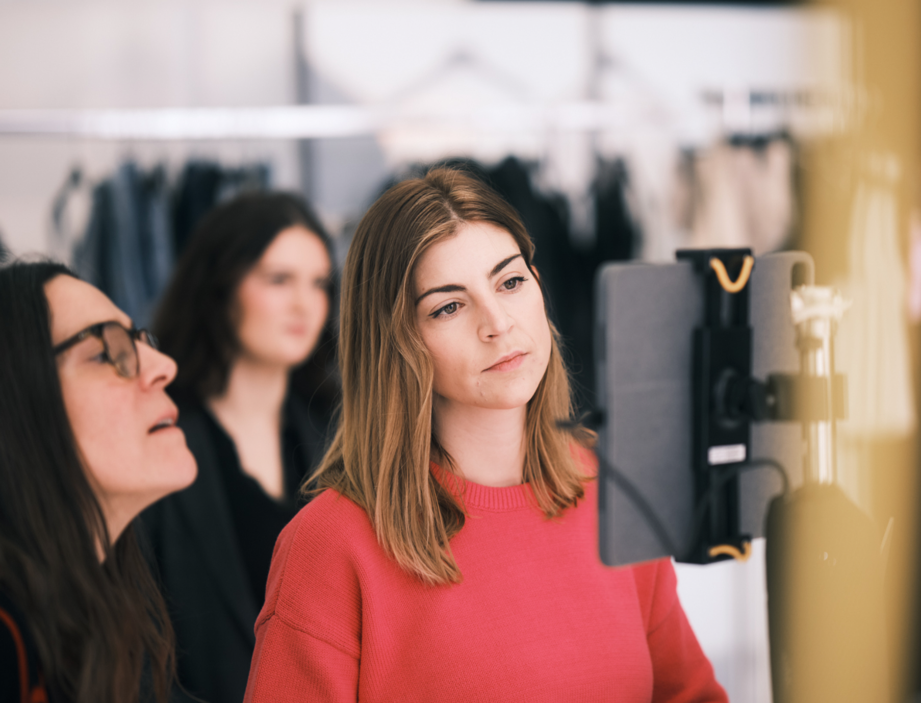 A smiling woman with long, wavy hair, wearing a blue striped shirt and earrings, looking at a silver Apple laptop.