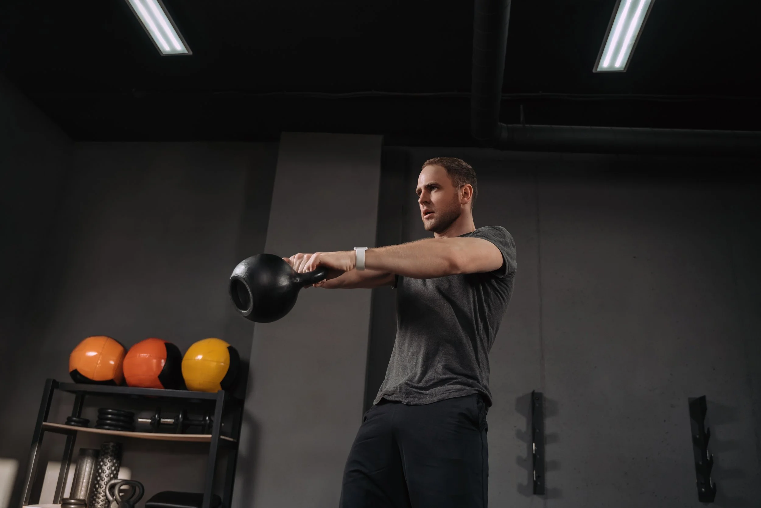 Man in a gym lifting a kettlebell with both hands.
