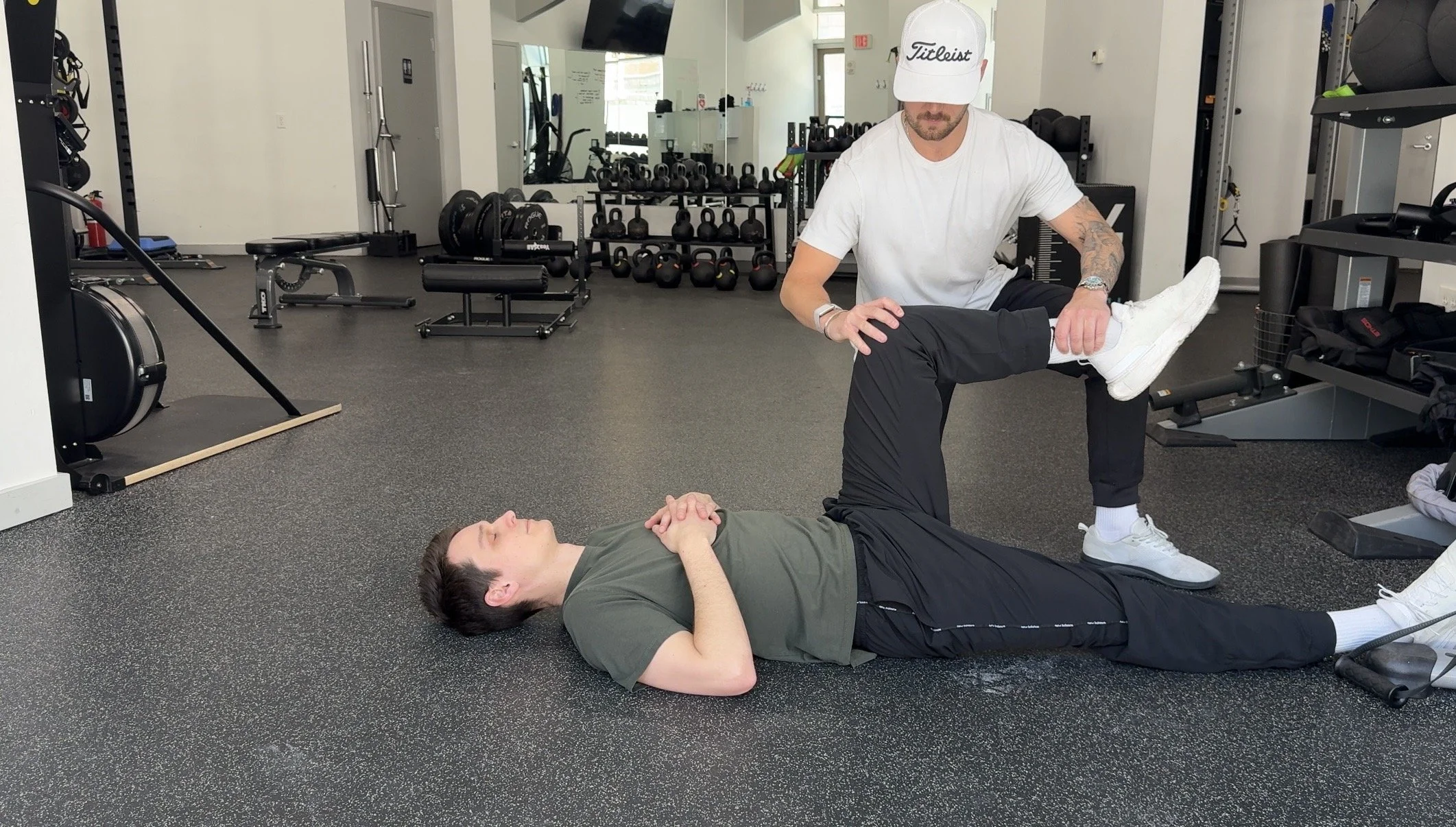 Doctor of Physical Therapy performing a hip mobility assessment on the floor inside a gym.