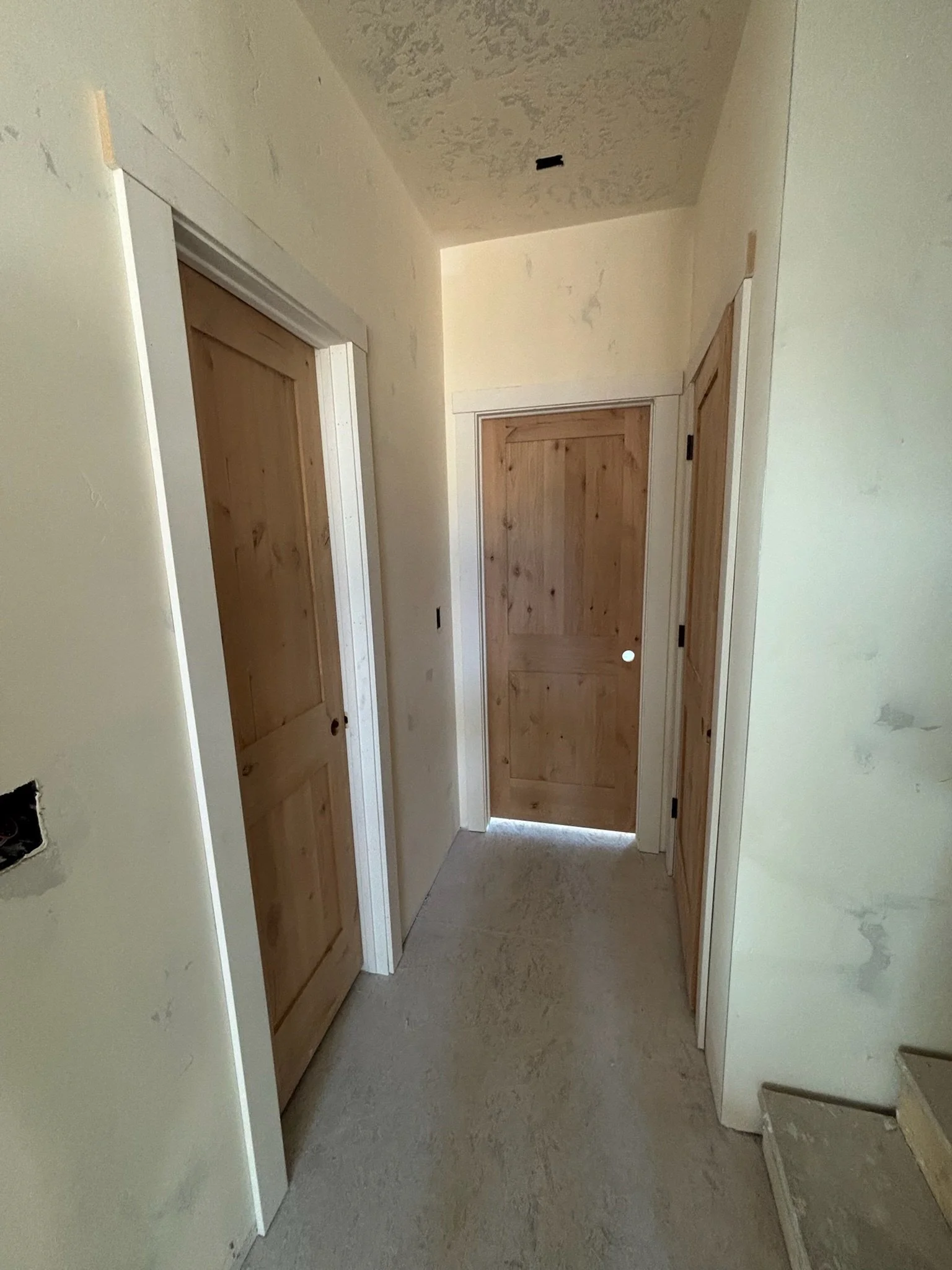Interior of a house under construction or renovation, showing doors and unfinished walls with visible drywall and an open electrical box.