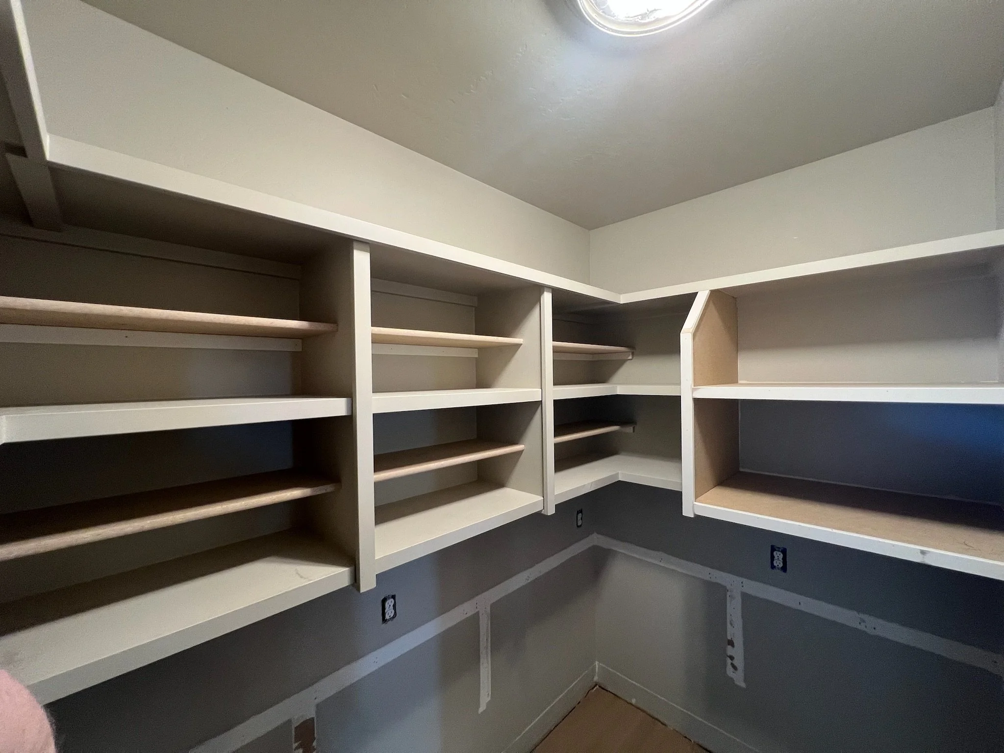 Empty white wood shelving units without items, located in a room with gray painted walls and a ceiling light fixture.