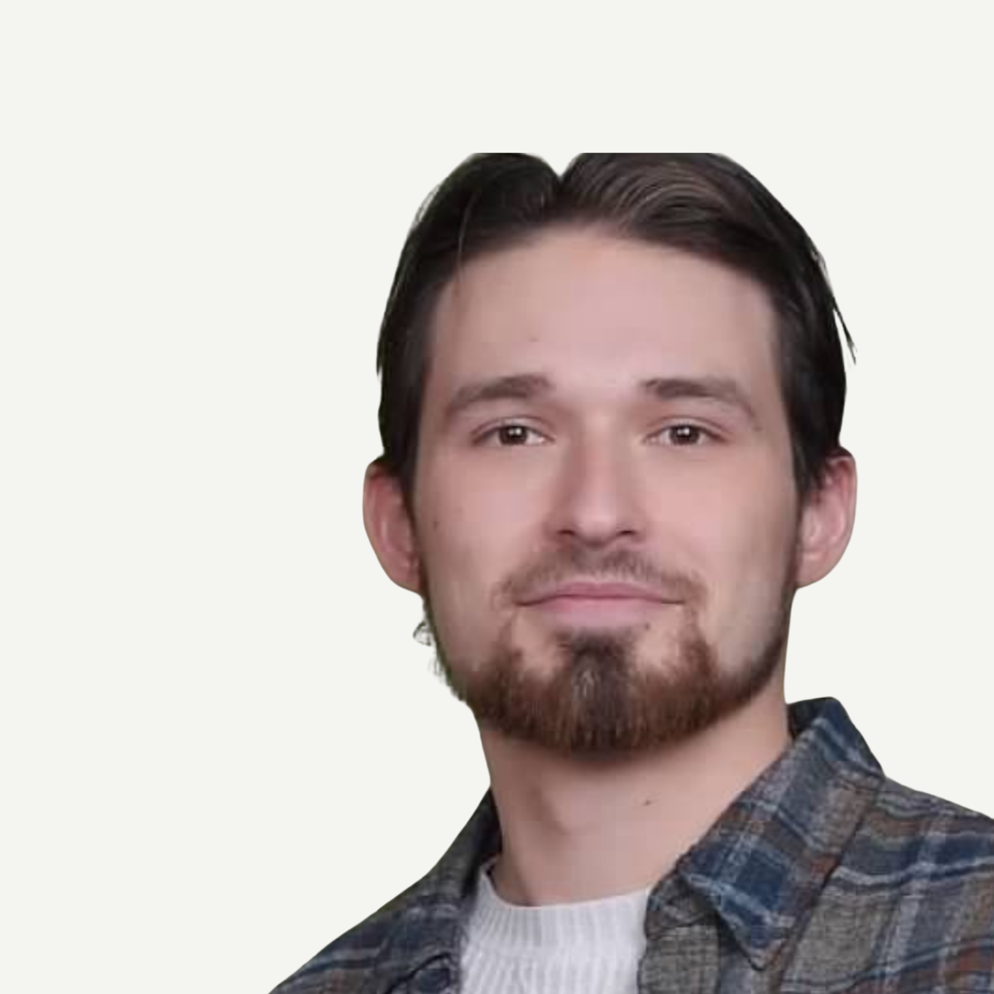 Close-up of a young man's face, showing his forehead, eyes, nose, and mouth, with dark hair and a beard, wearing a plaid shirt over a white t-shirt.