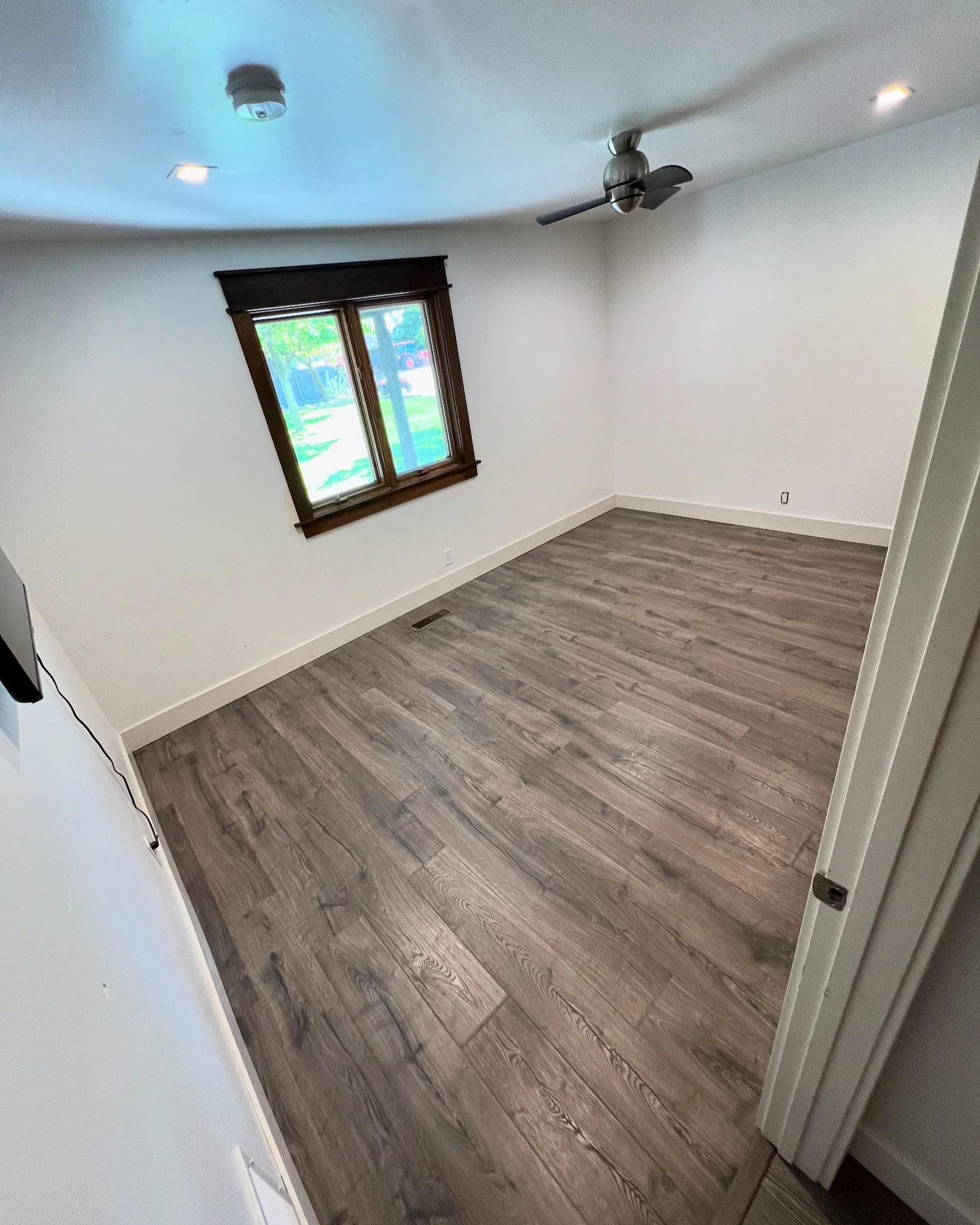 Empty room with a large window, wooden crown molding, ceiling fan, hardwood flooring, and white walls.