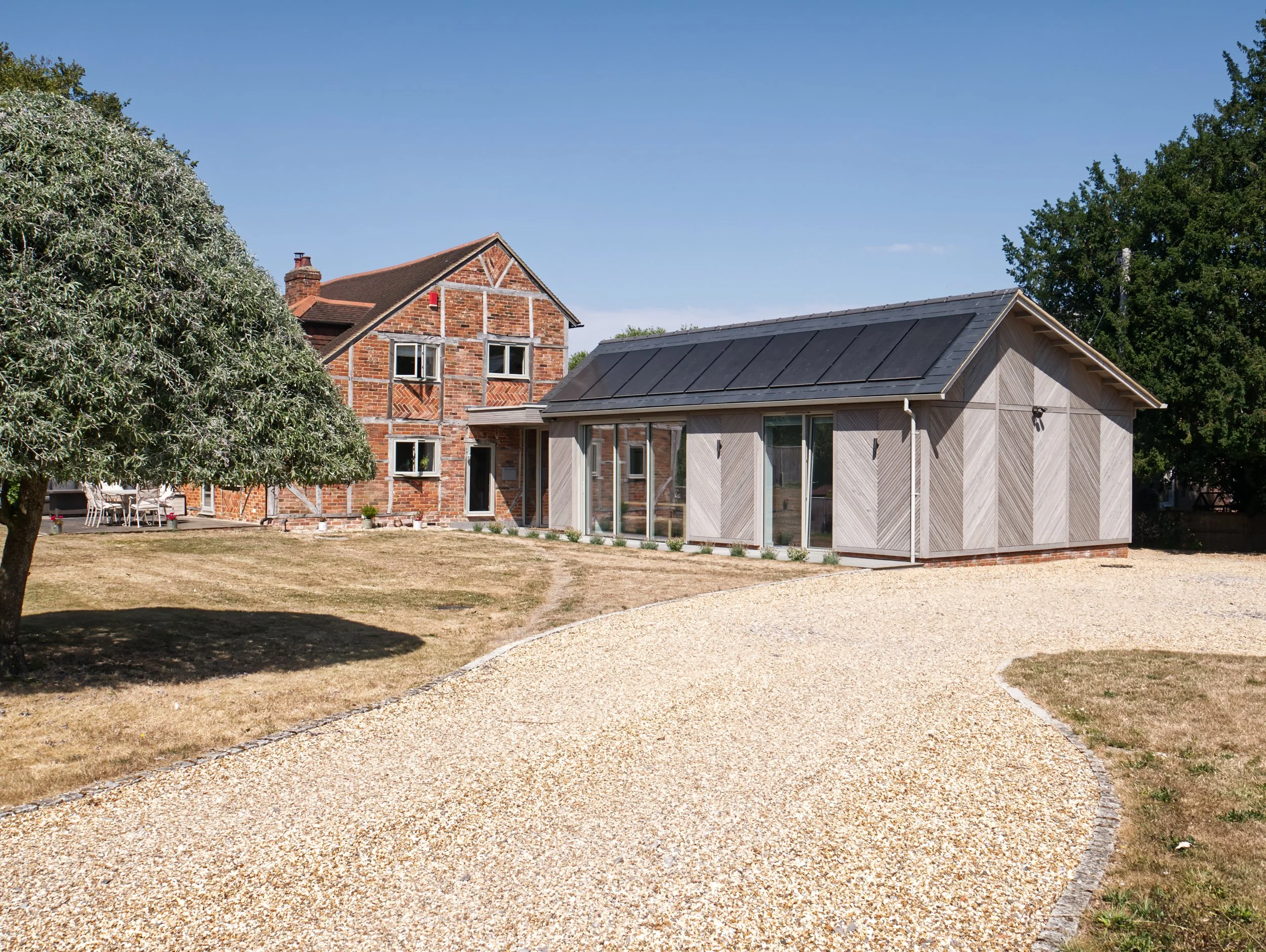 modern extension with grey chevron timber cladding, herringbone brickwork, a slate roof and flush solar panels