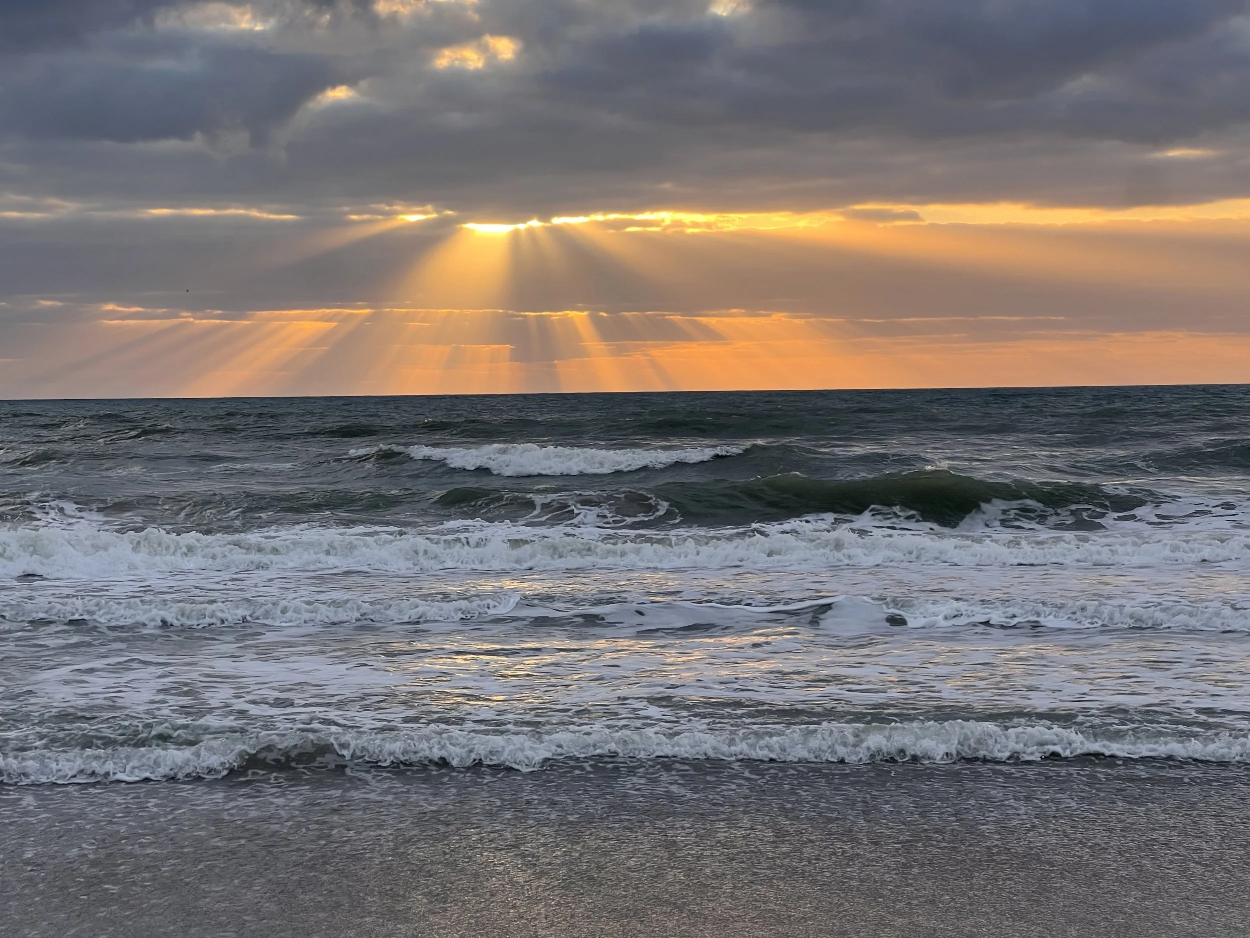 Sunset over the ocean with rays of sunlight peeking through clouds and waves crashing on the shore. Strategic Communication and Marketing on Florida's Space Coast/Brevard County.