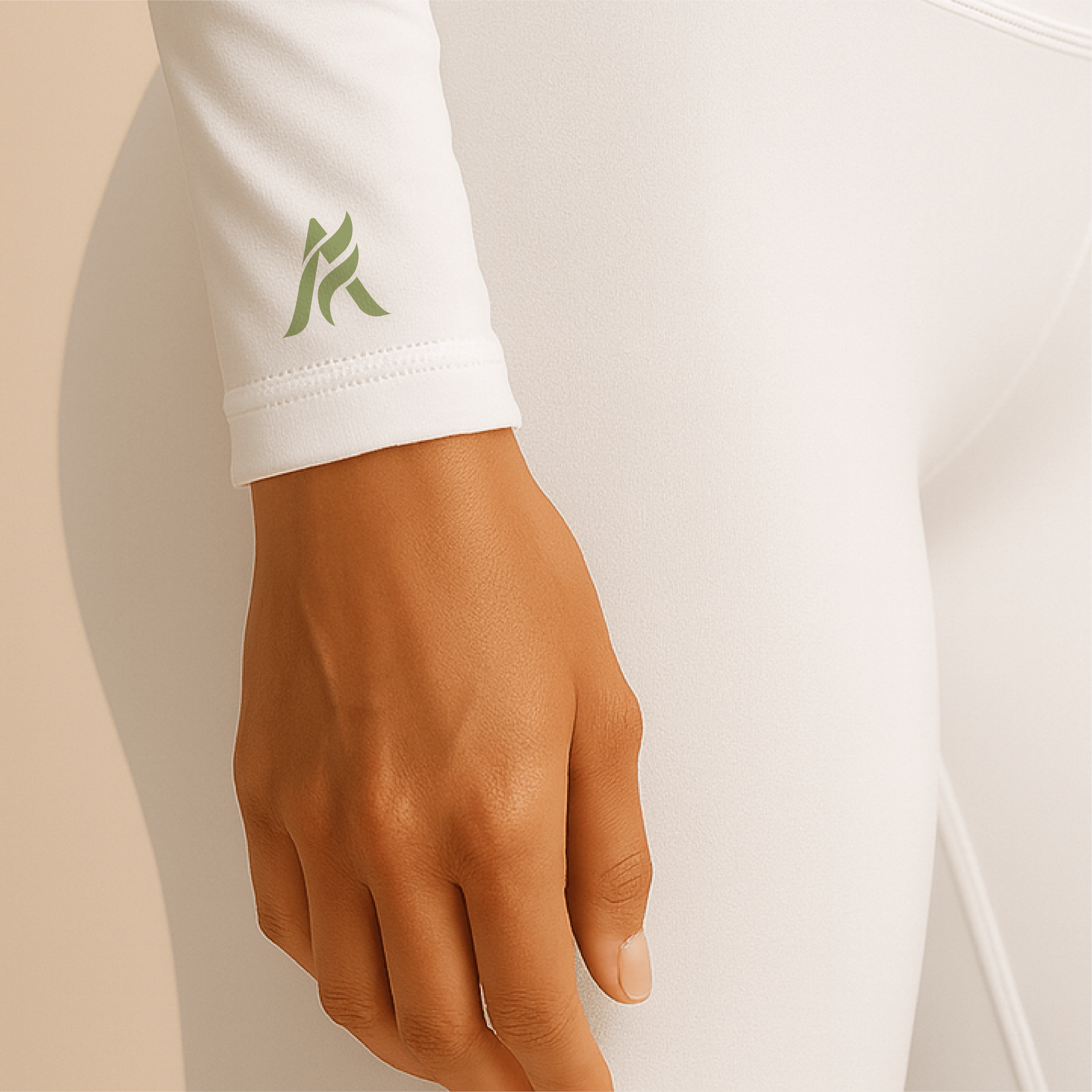 Close-up of a person's hand resting on their hip, wearing a white long-sleeve garment with a small green logo on the sleeve, and white pants.