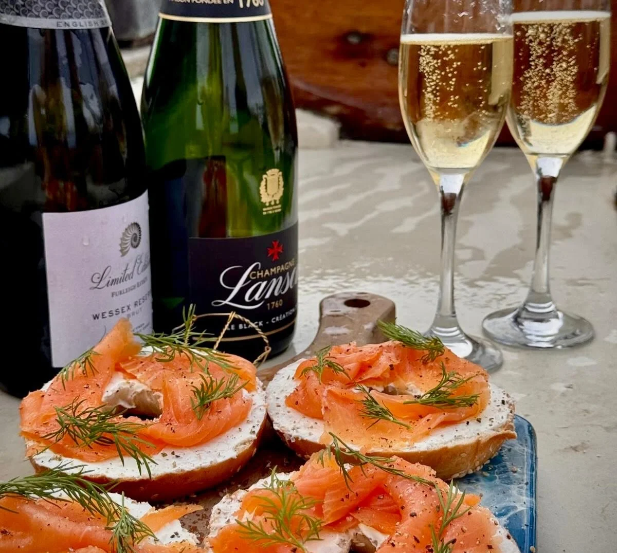 Open-faced smoked salmon bagels with dill, bottles of champagne, and glasses of sparkling wine on a table.