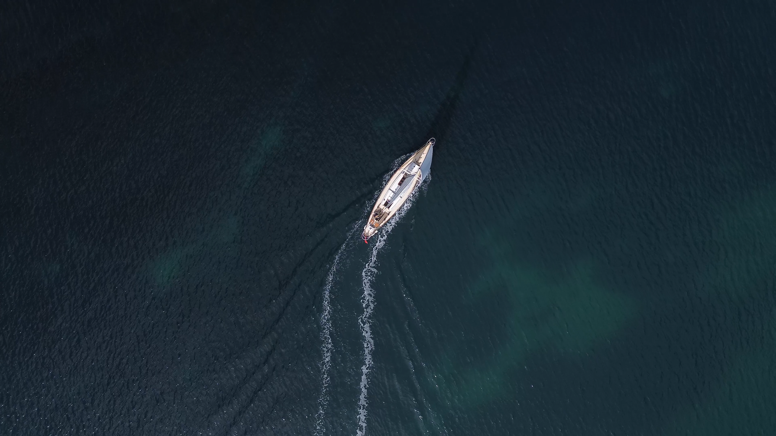 A sailboat with a white hull sailing on dark blue water, creating a wake behind it.