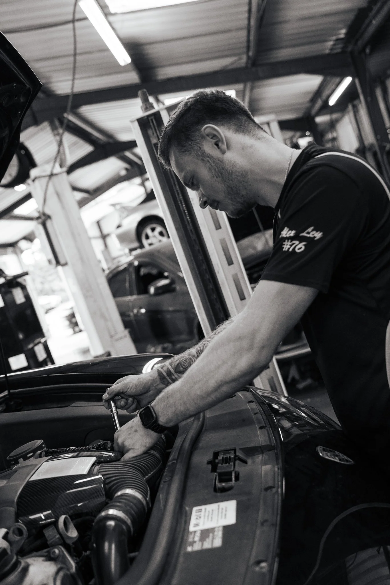 A young mechanic working underneath a car with its hood open in a garage.