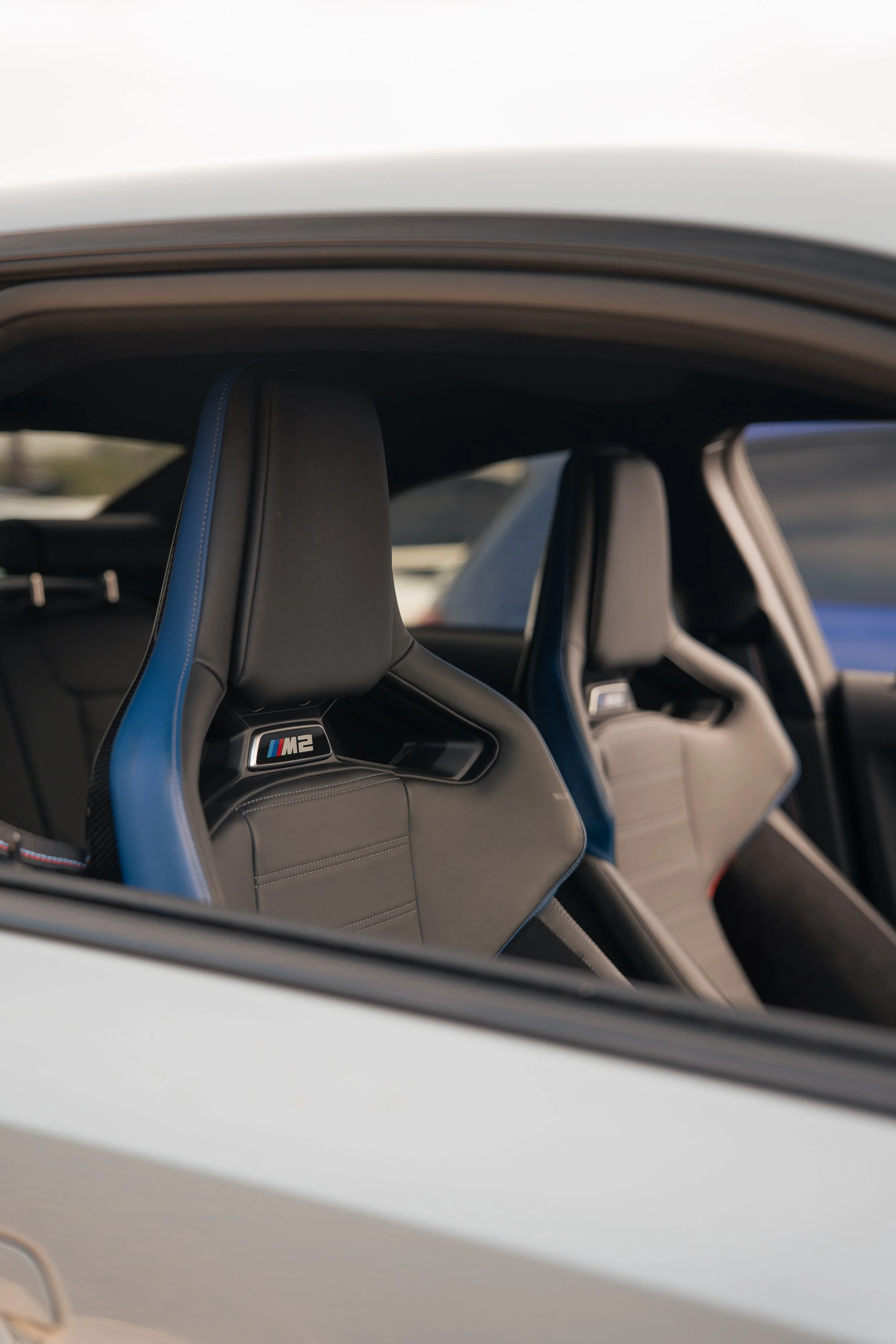 Close-up of the interior of a BMW M2 sports car, featuring black racing seats with blue accents and the M2 logo on the headrests.