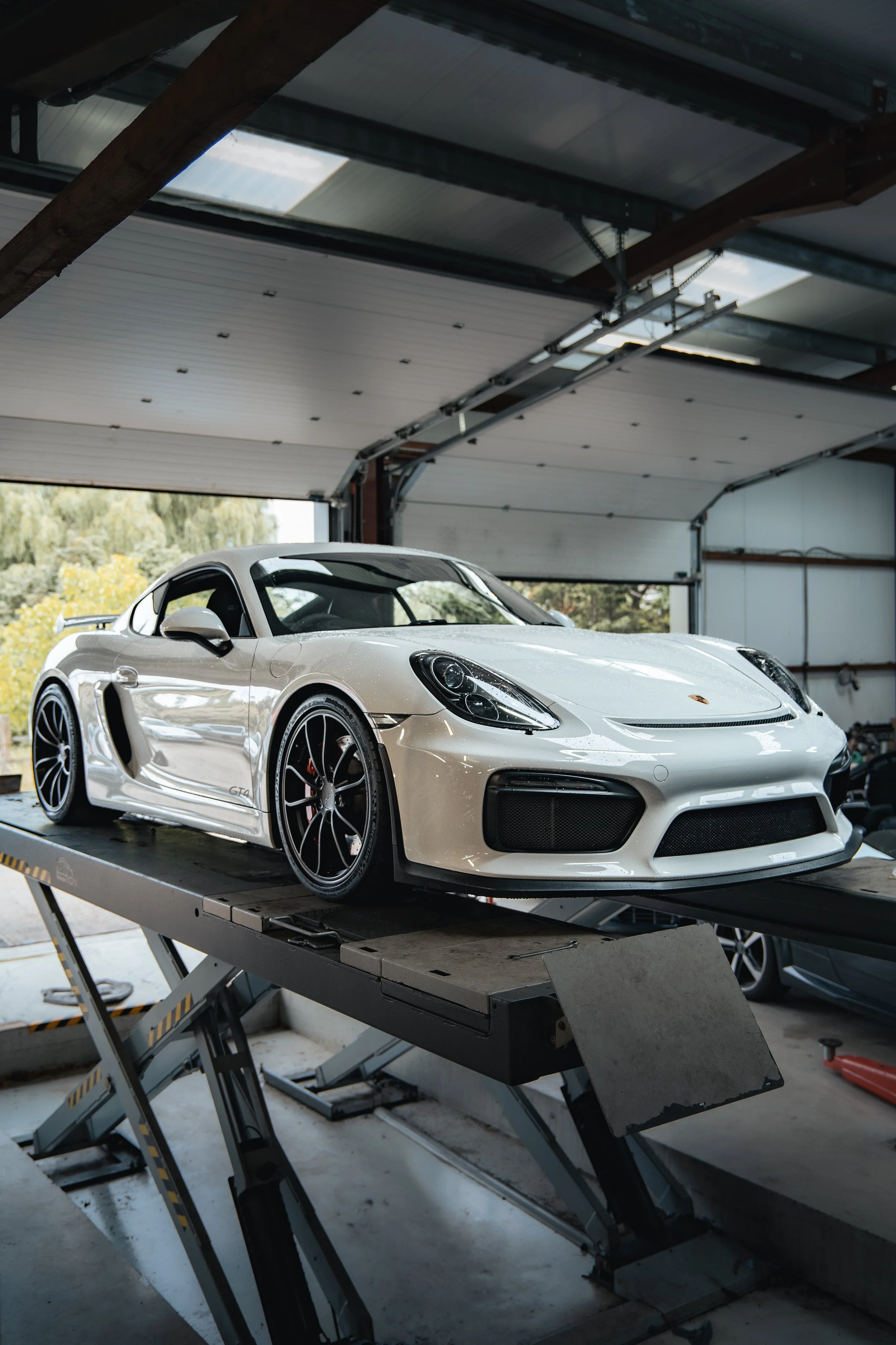 A white Porsche 718 Cayman GT4 sports car on a Hunter 4 Wheel Alignment Machine in the workshop