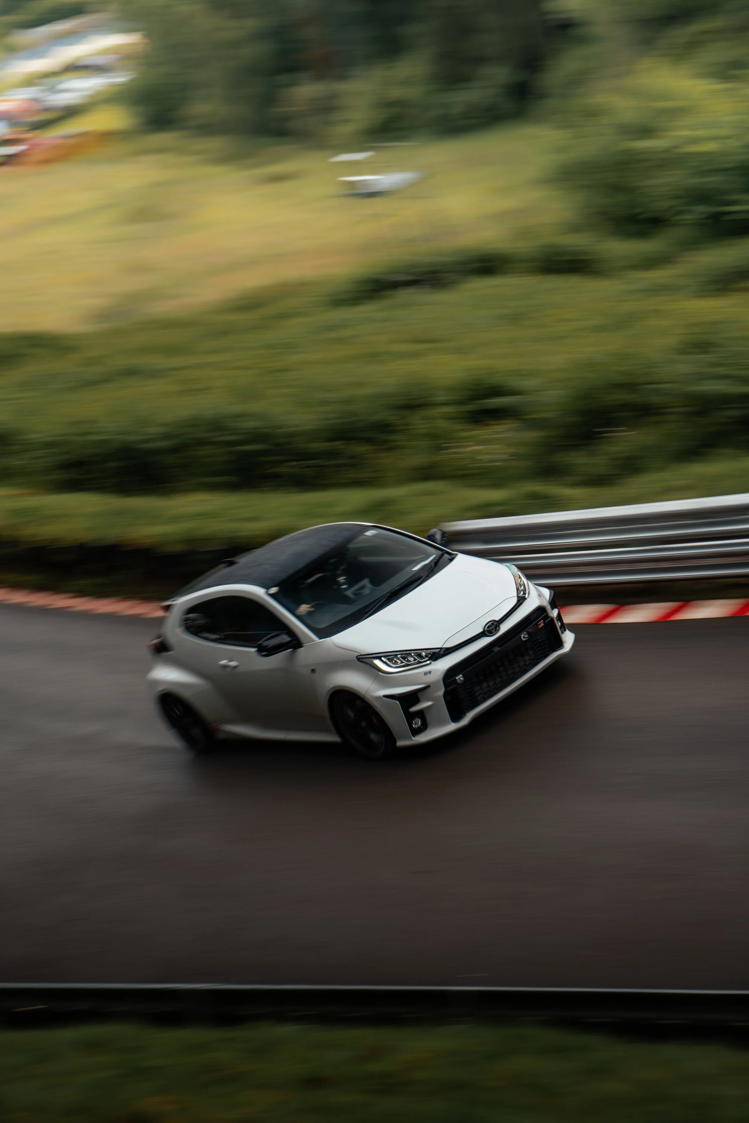 A silver racing car driving at high speed on a curvy road with green trees in the background, creating a motion blur effect.