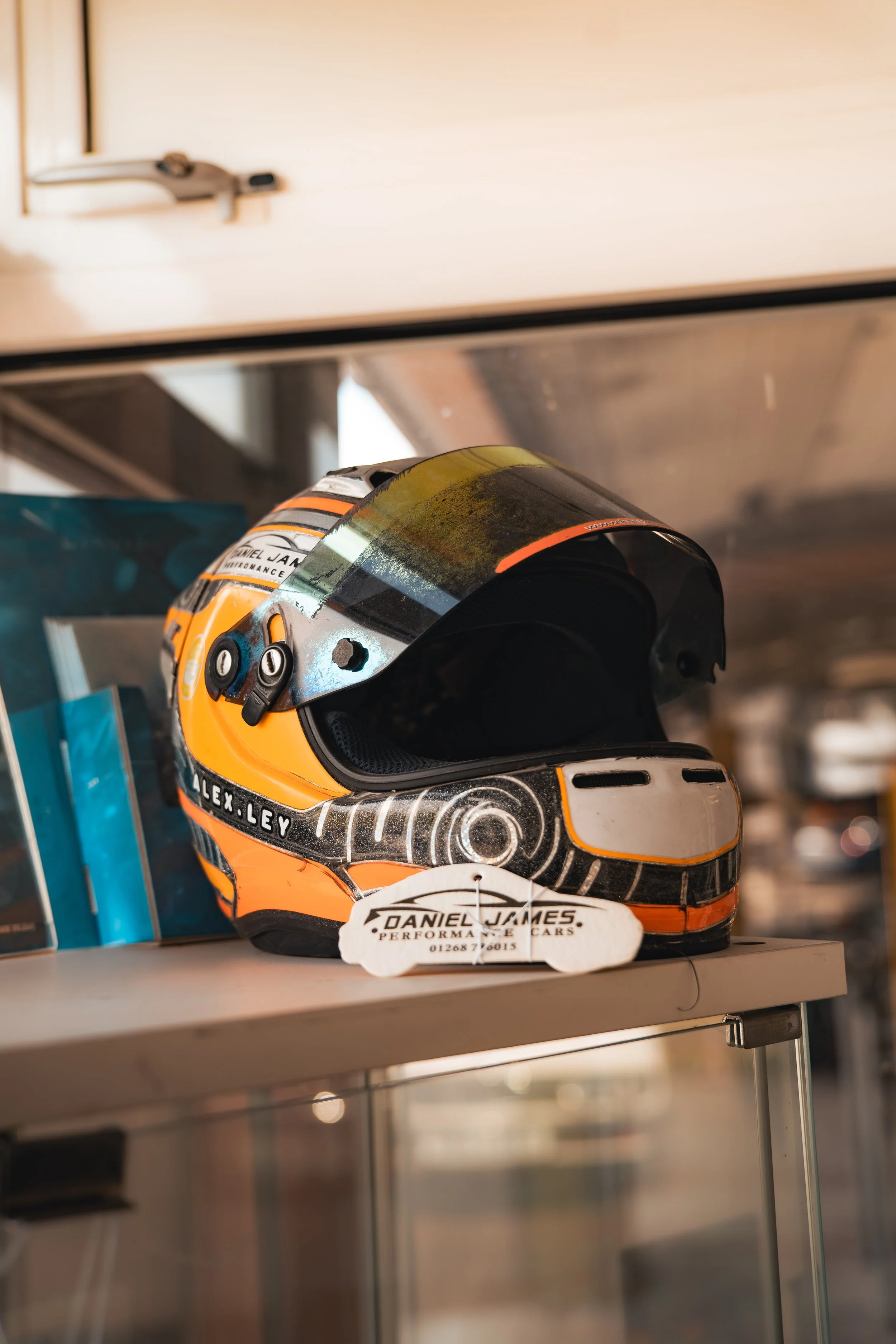Race car helmet with orange, black, and white design on display on a shelf
