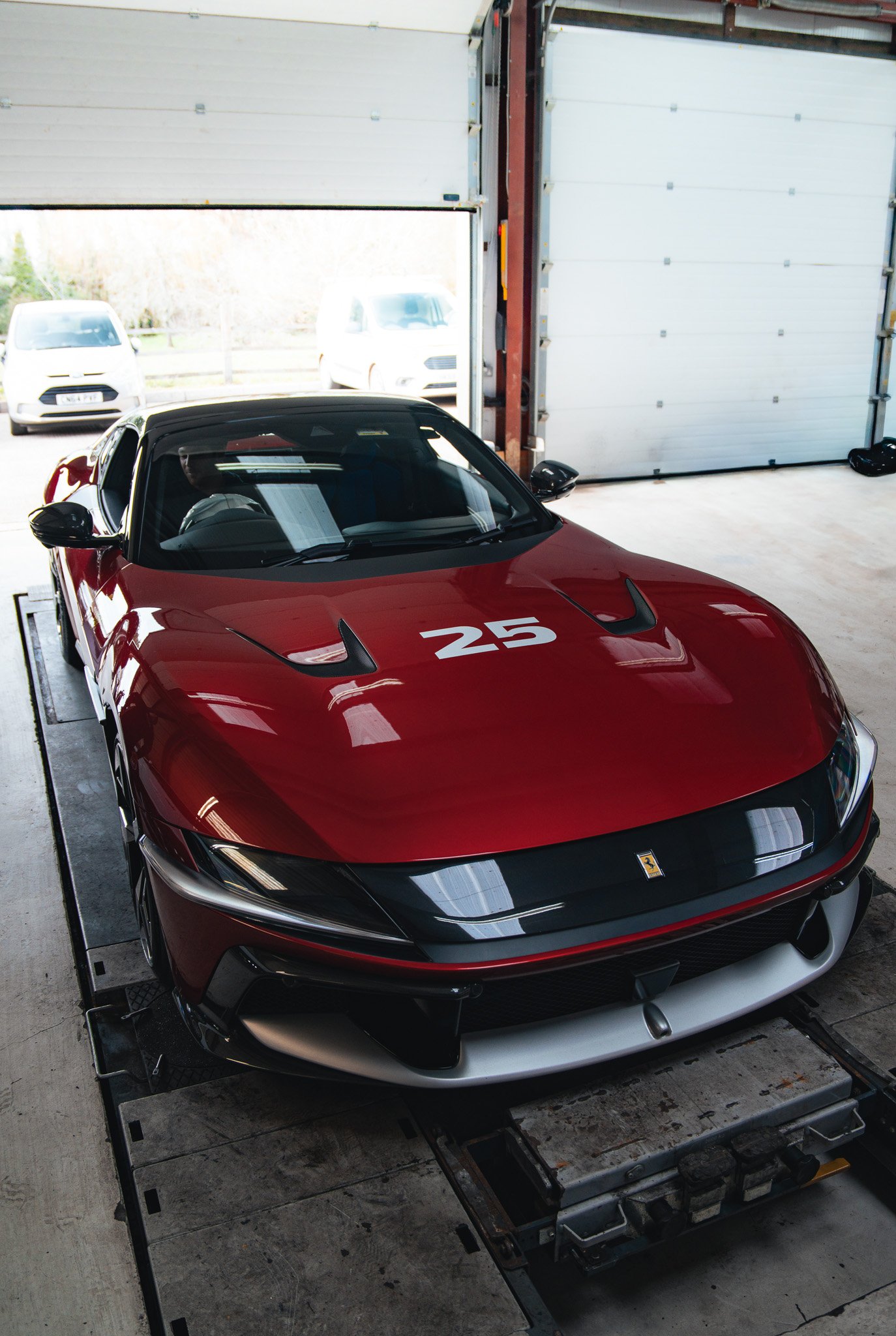 Red rally car on a dynamometer testing stand in a garage, with wheel alignment equipment attached.