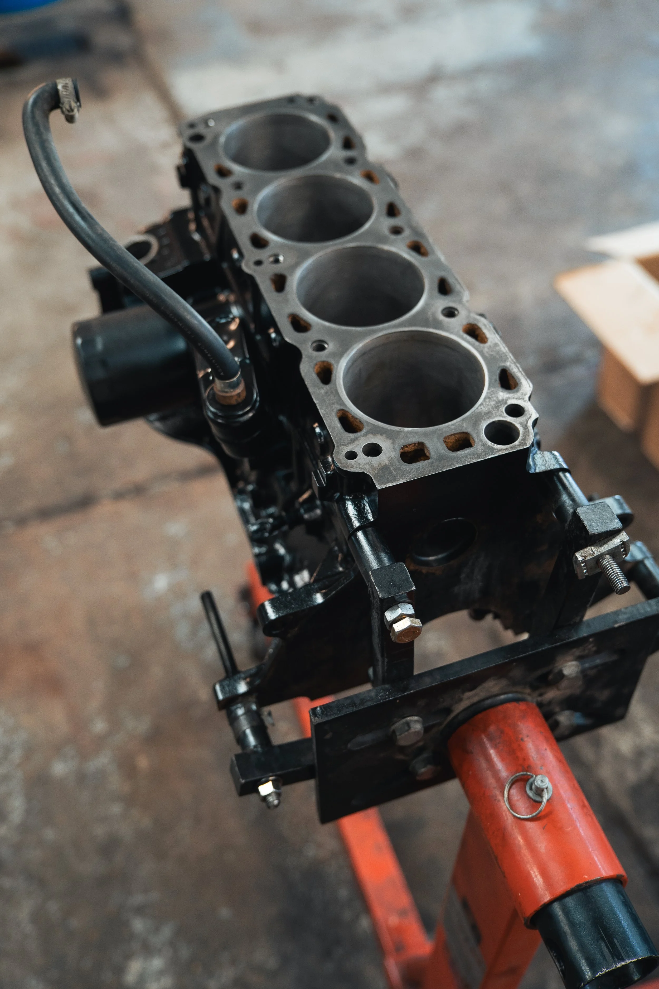 An engine cylinder block mounted on a red stand, with the cylinder head removed revealing four cylinders.