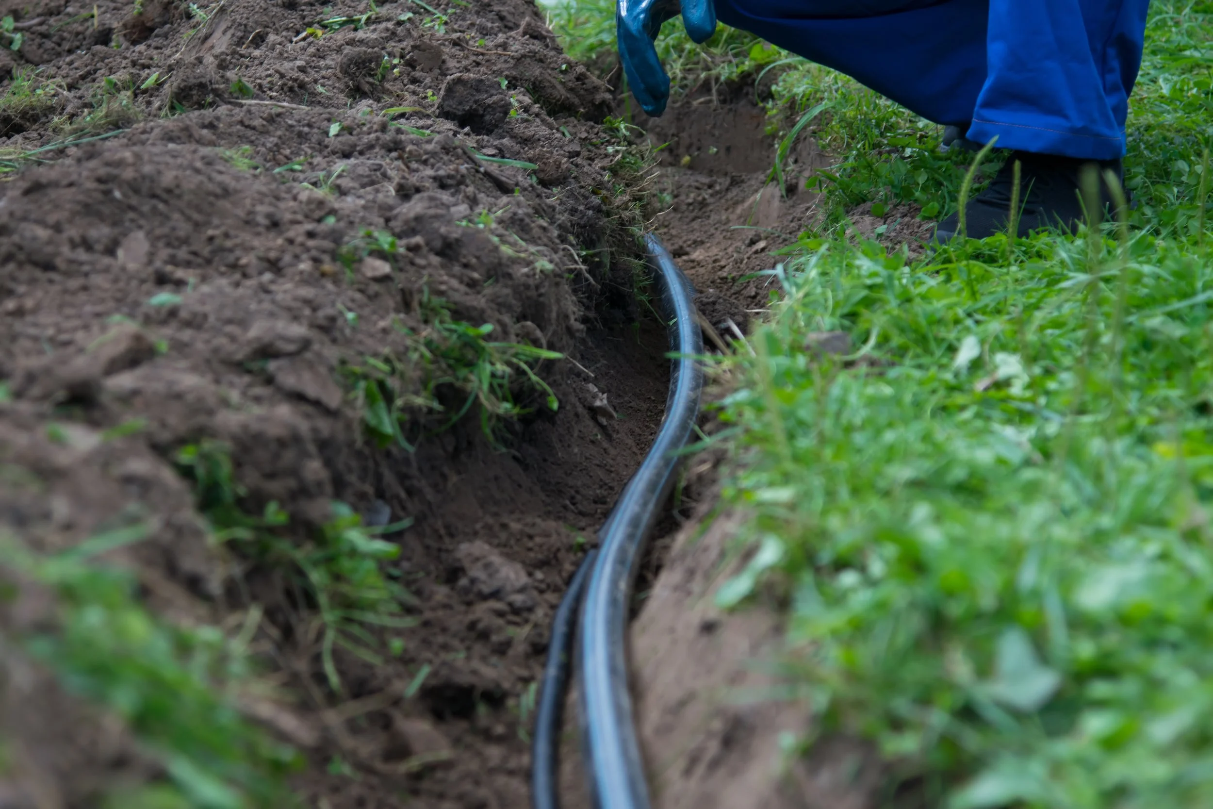 Cable in a trench with grass and soil, person in blue work attire