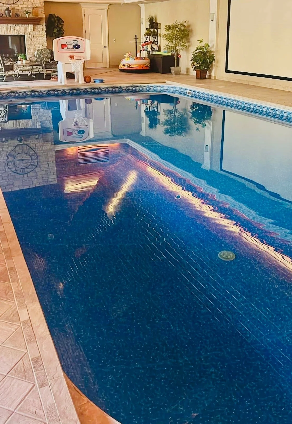 Indoor swimming pool with a reflection of a colorful neon light strip and a basketball hoop in the background.