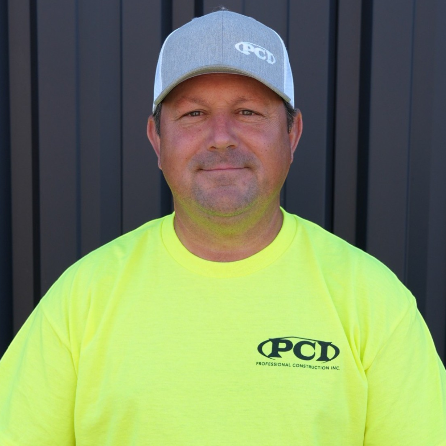 Portrait of a man wearing a black PPC hat and a black PPC t-shirt standing in front of a dark grey wall.
