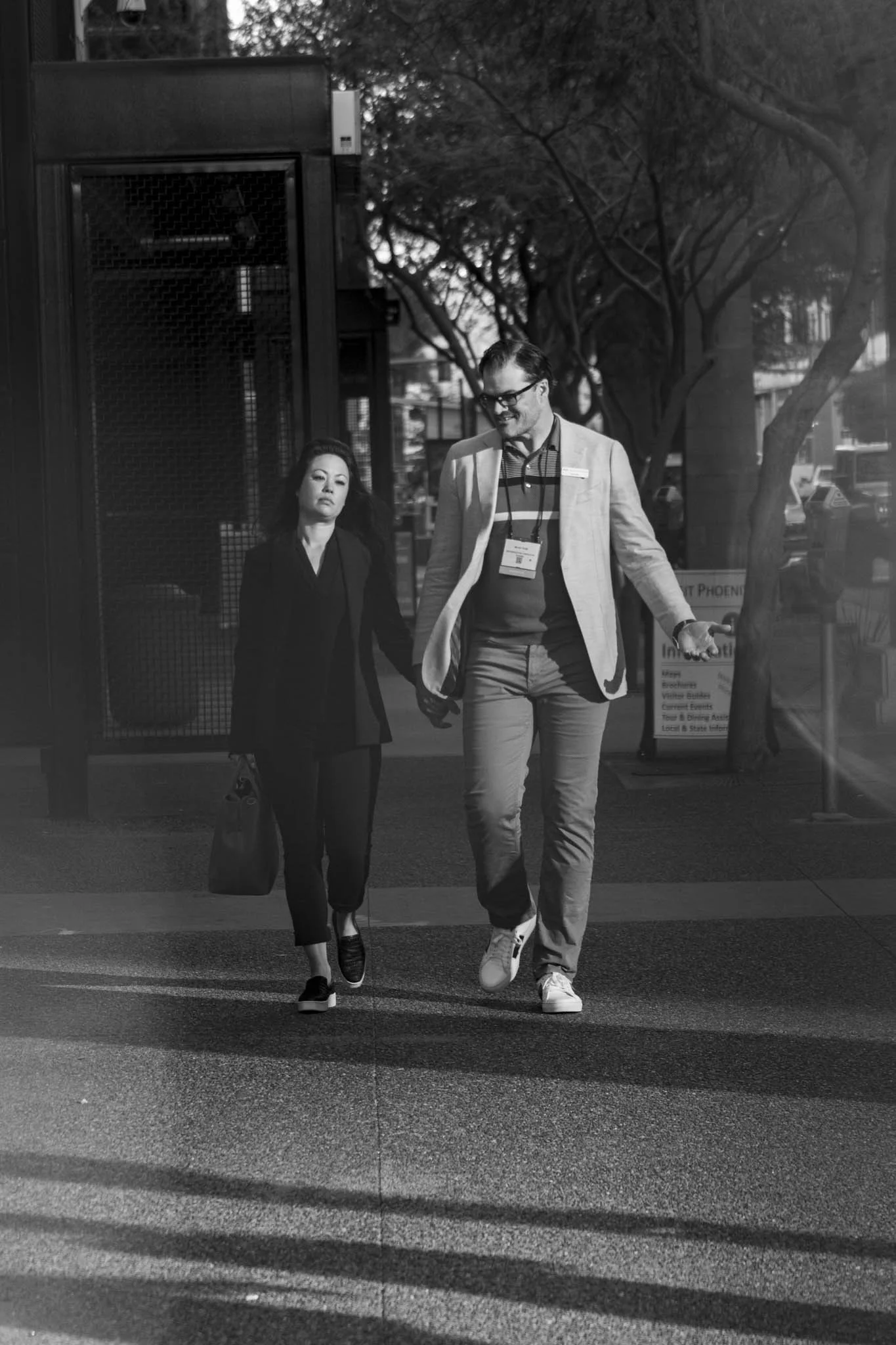 Two people walking across a crosswalk in an urban area. One woman and one man, both dressed professionally. The image is in black and white.