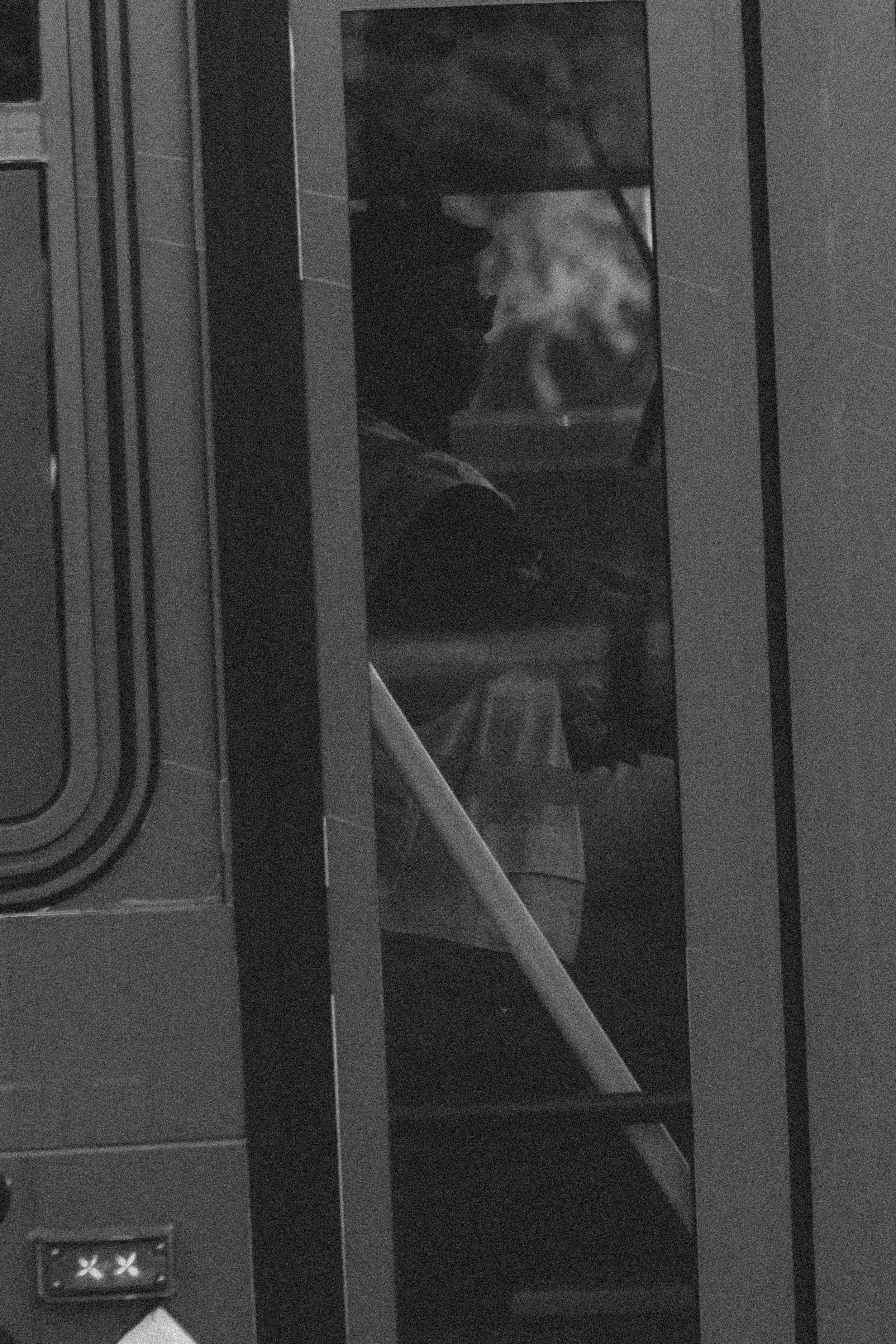 A person sitting inside a small, enclosed space, possibly a vending machine or phone booth, seen through a glass window, with some smoke or vapor around them.