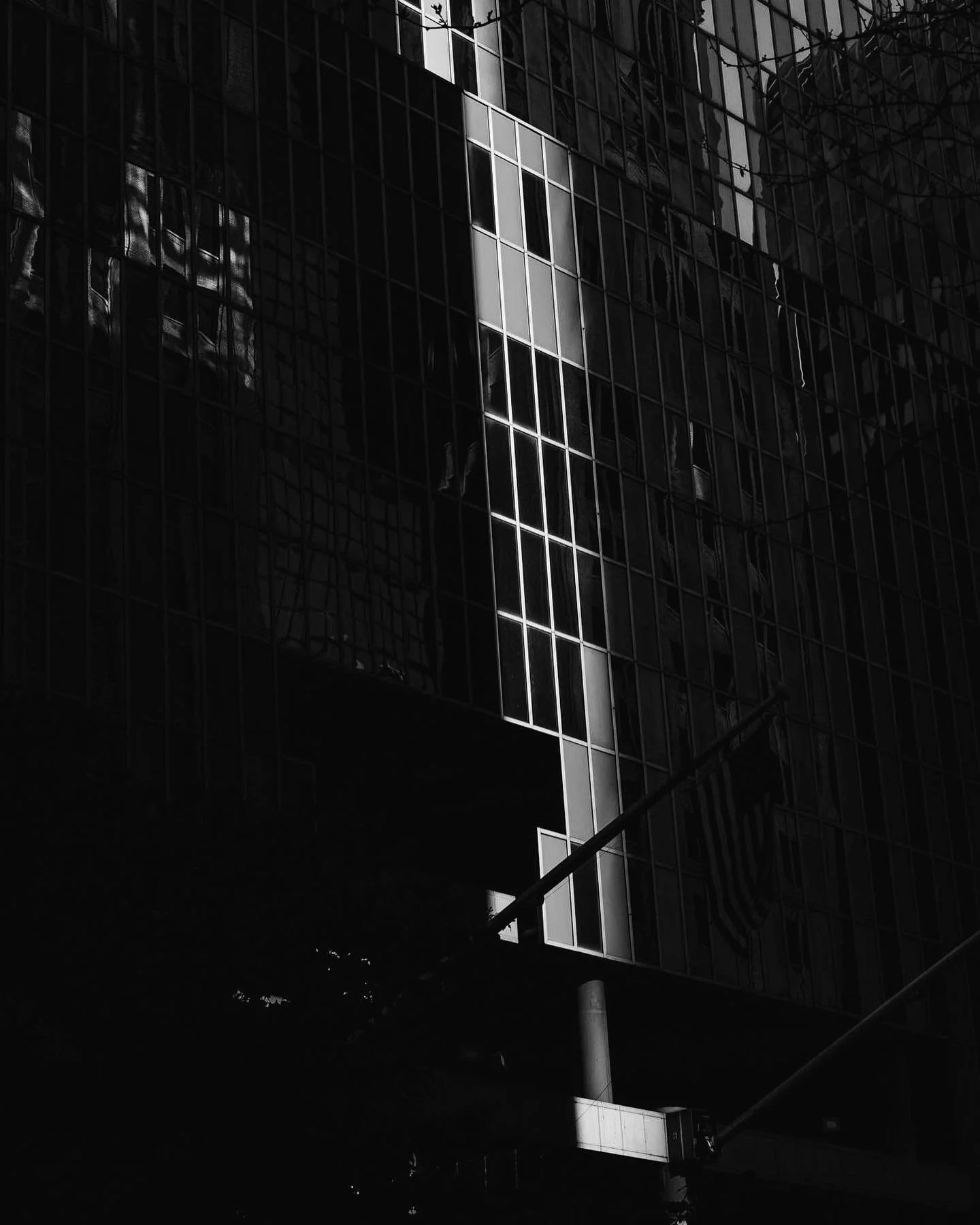 A tall modern glass building with dark reflective windows, some of which reveal an interior view with visible objects and lights. There is a partially visible American flag hanging outside, and the image is in black and white.
