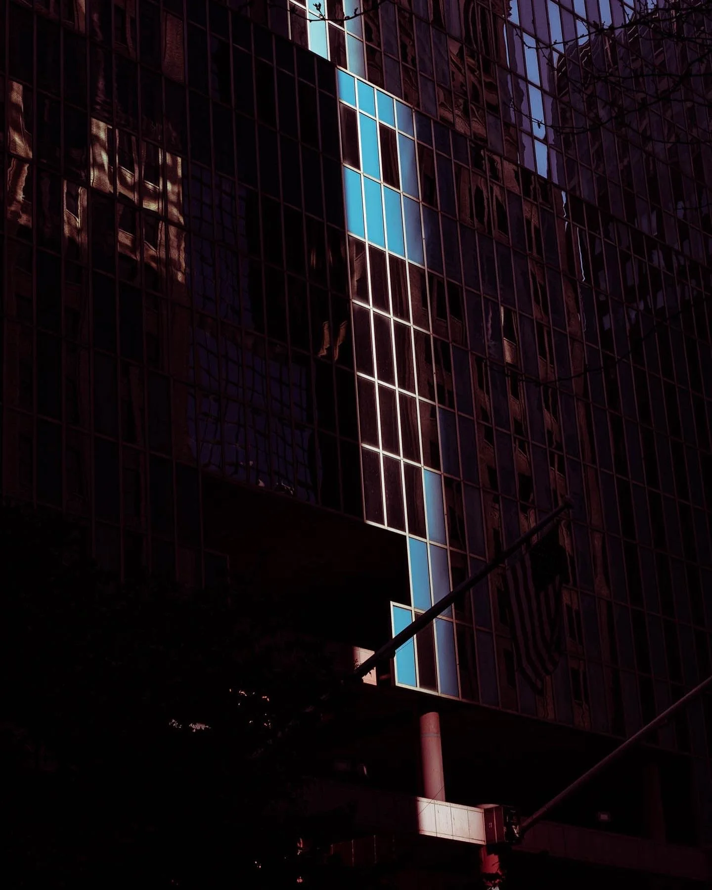 Close-up of a tall building with glass windows, some with a blue tint, reflecting nearby structures, with street signs and poles in the foreground.
