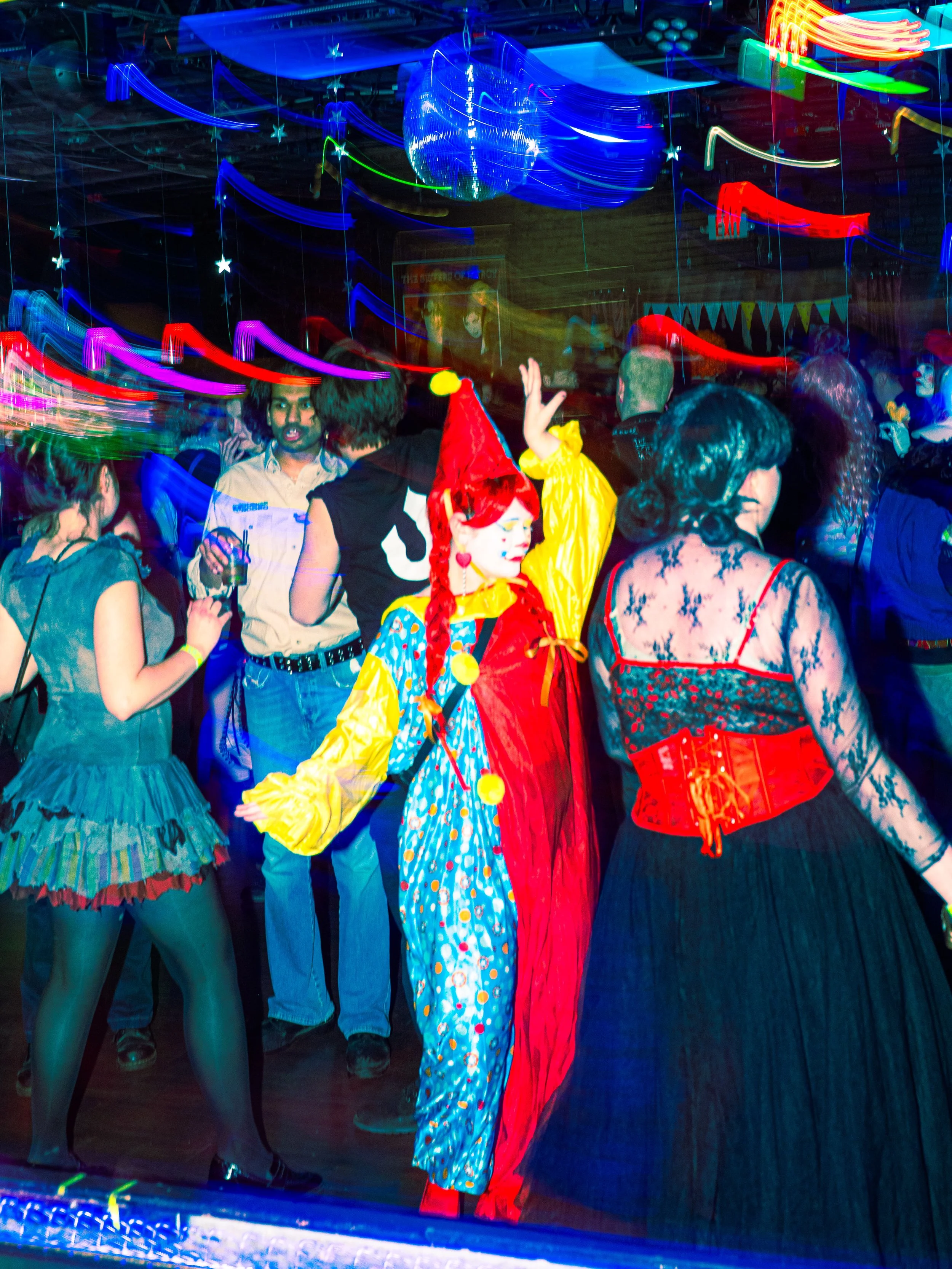 People dressed in colorful costumes dancing at a neon-lit party with blurred light trails and decorations.