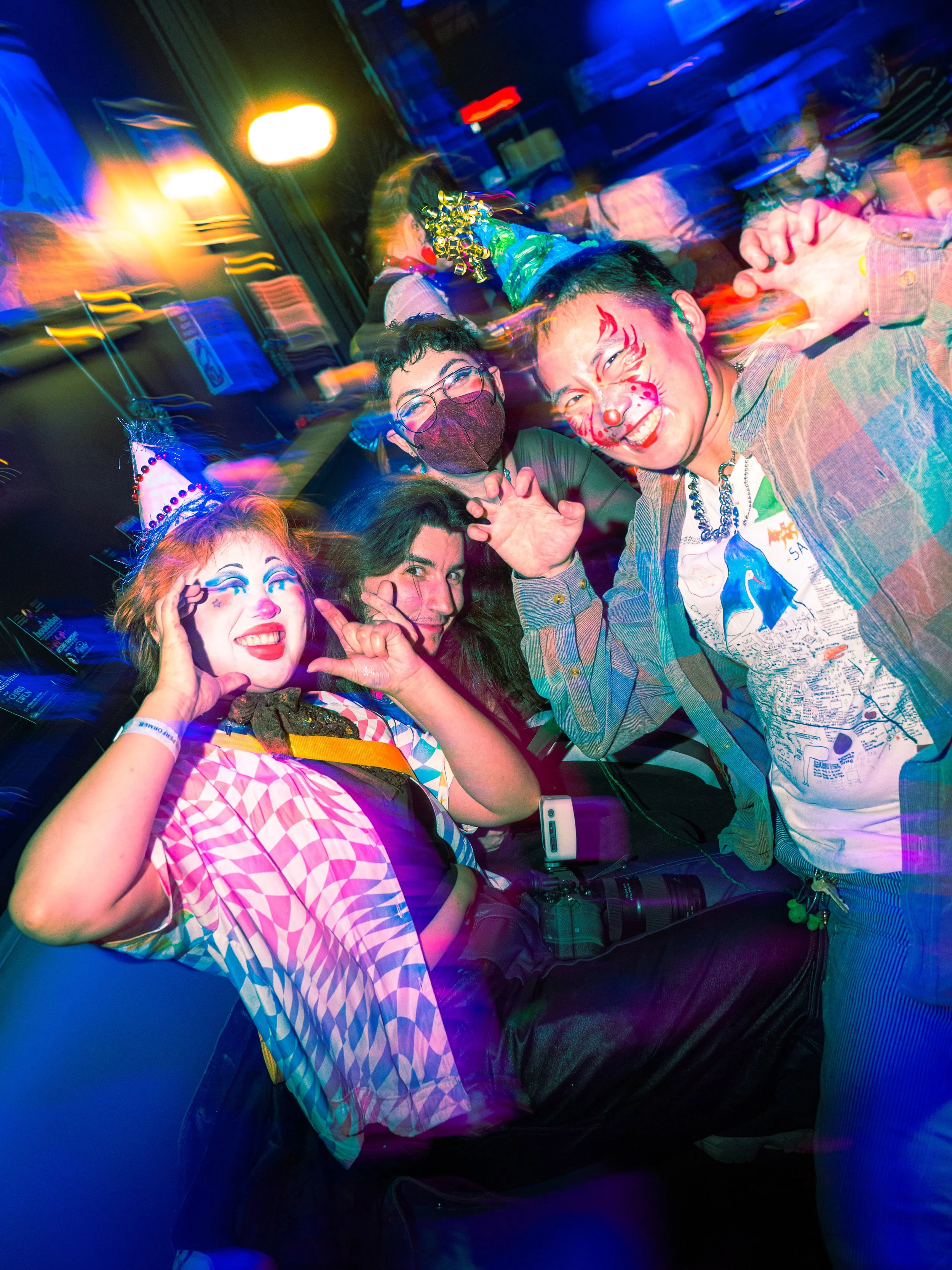 Group of people dressed in colorful costumes celebrating at a party, with festive and playful expressions, some with face paint and accessories.