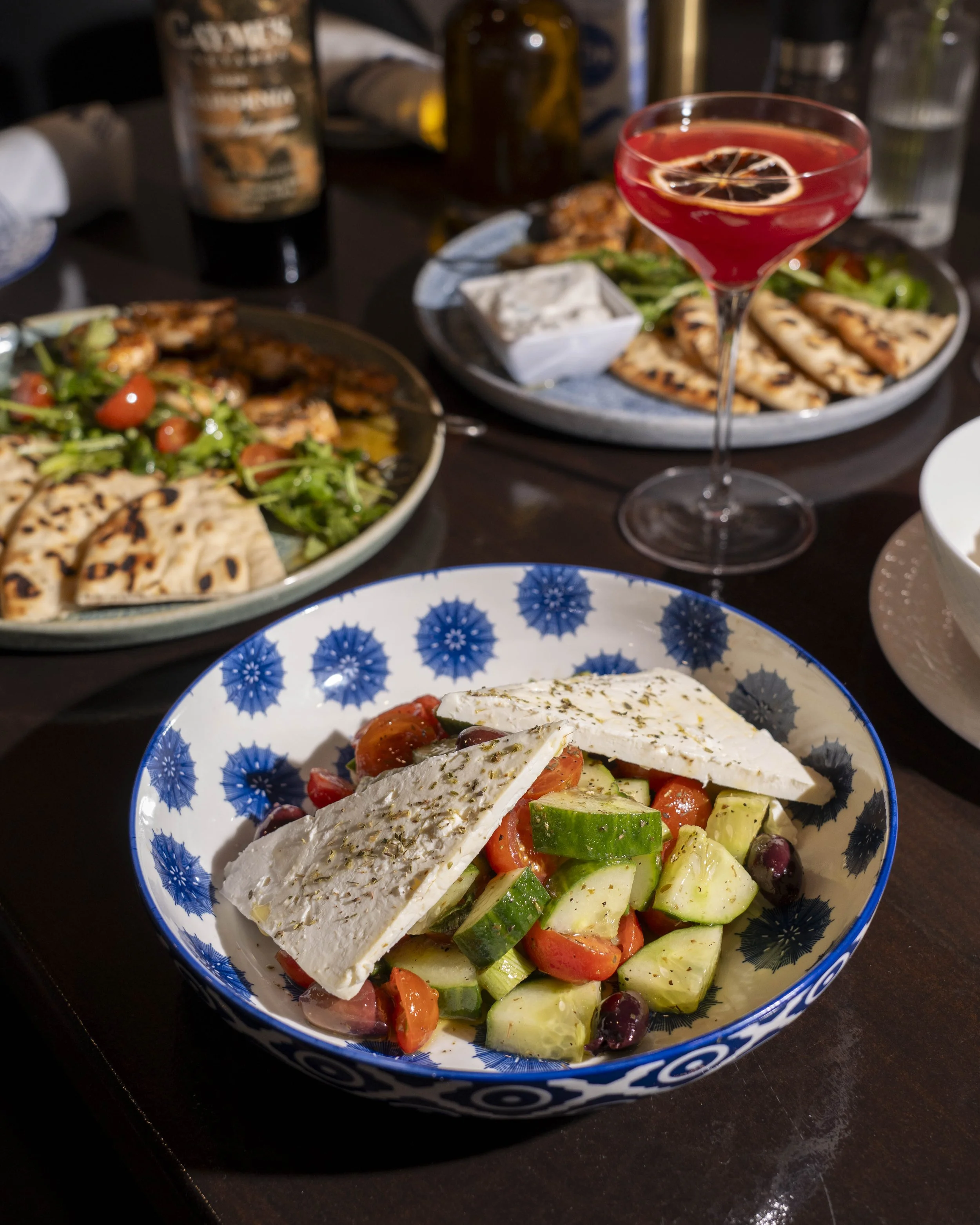 Salad with cherry tomatoes, cucumber, olives, and feta cheese on a patterned bowl.