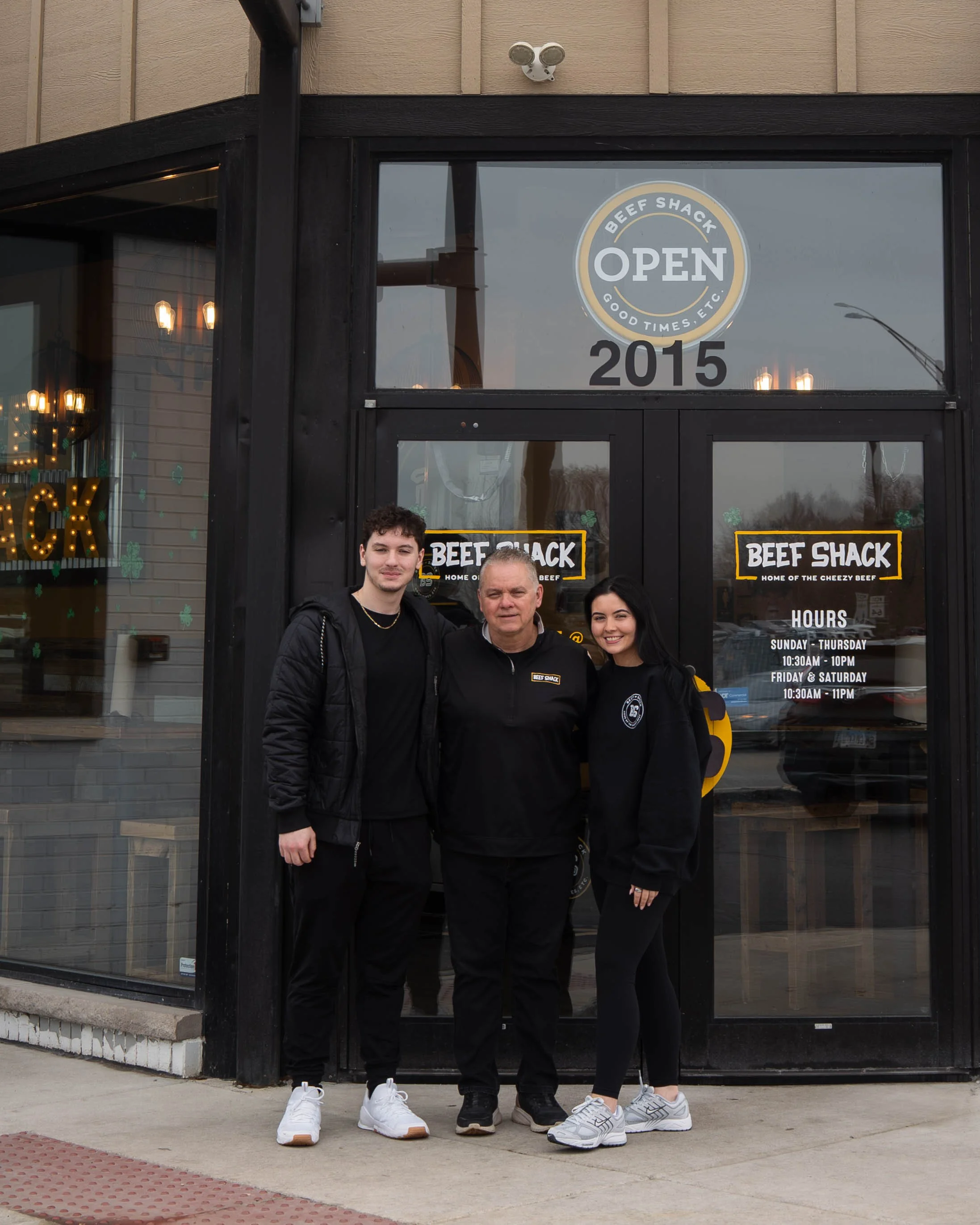 Three people standing outside a beef shack restaurant, smiling for the camera.